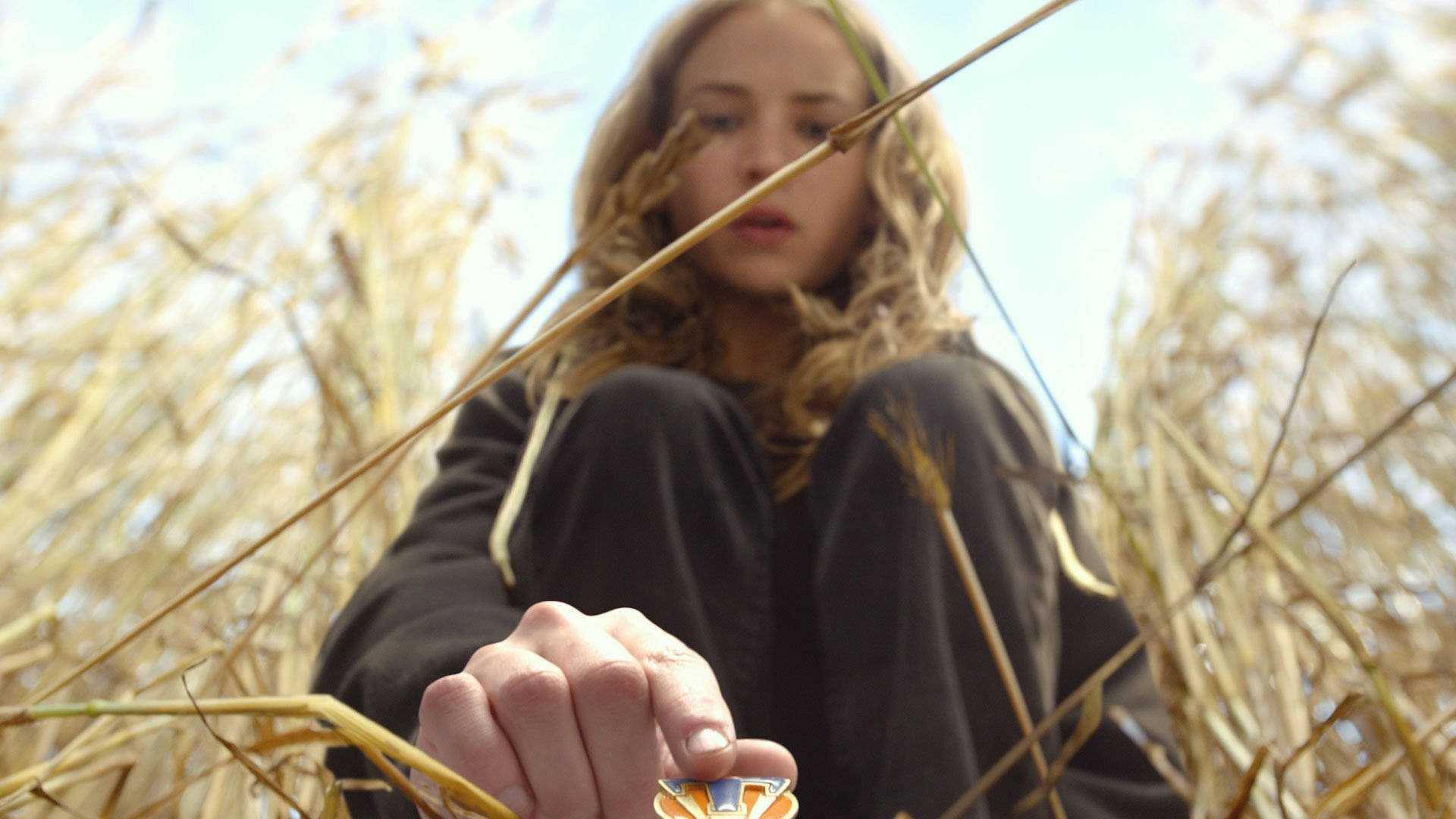 Tomorrowland Movie 桌布 壁紙 — 一位年輕女性坐在高高的金色草叢中，專注地拿著一個色彩繽紛的小物件。