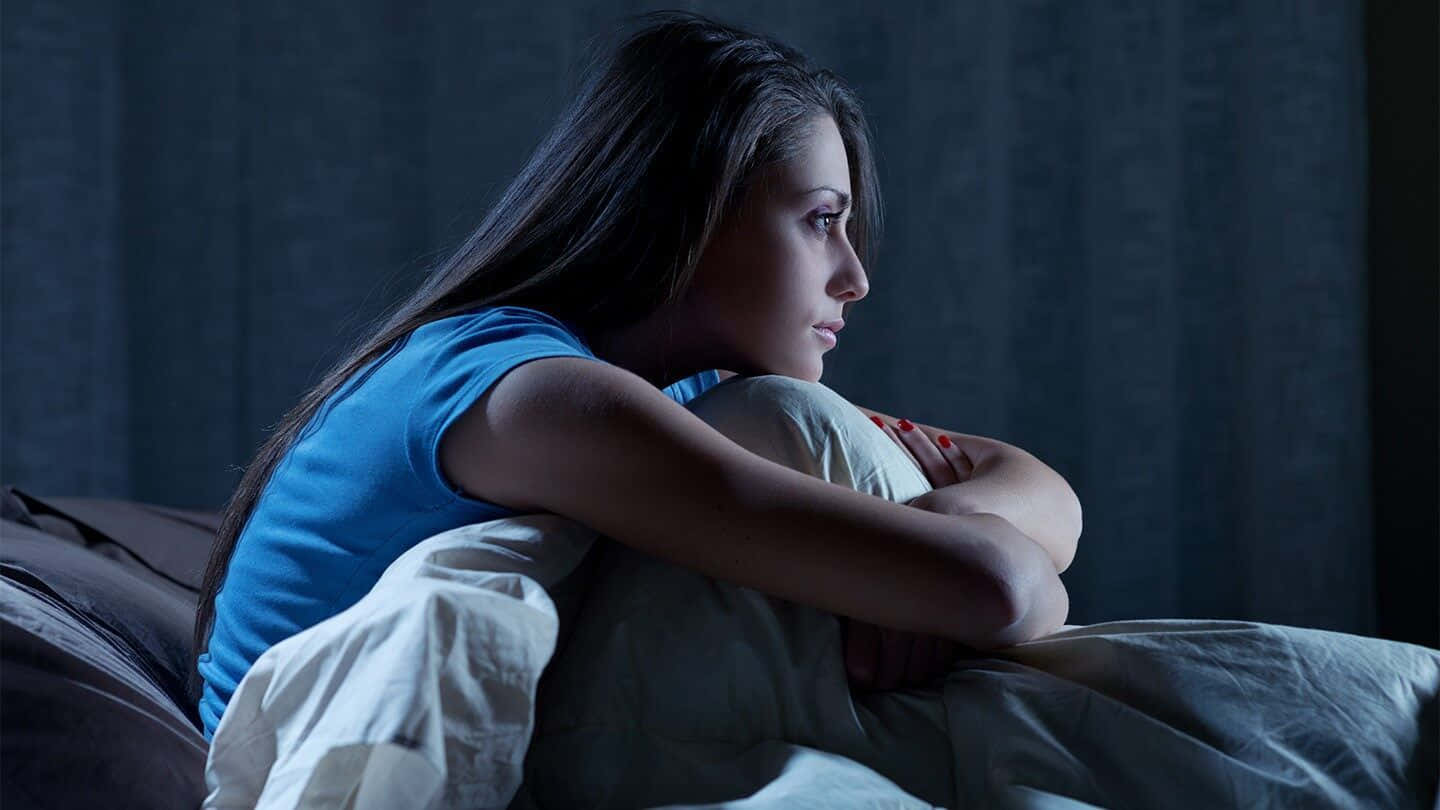 Lonely 桌布 壁紙 — 一位年輕女性夜晚獨自坐在床上，裹著毯子，在昏暗的藍光中沉思。