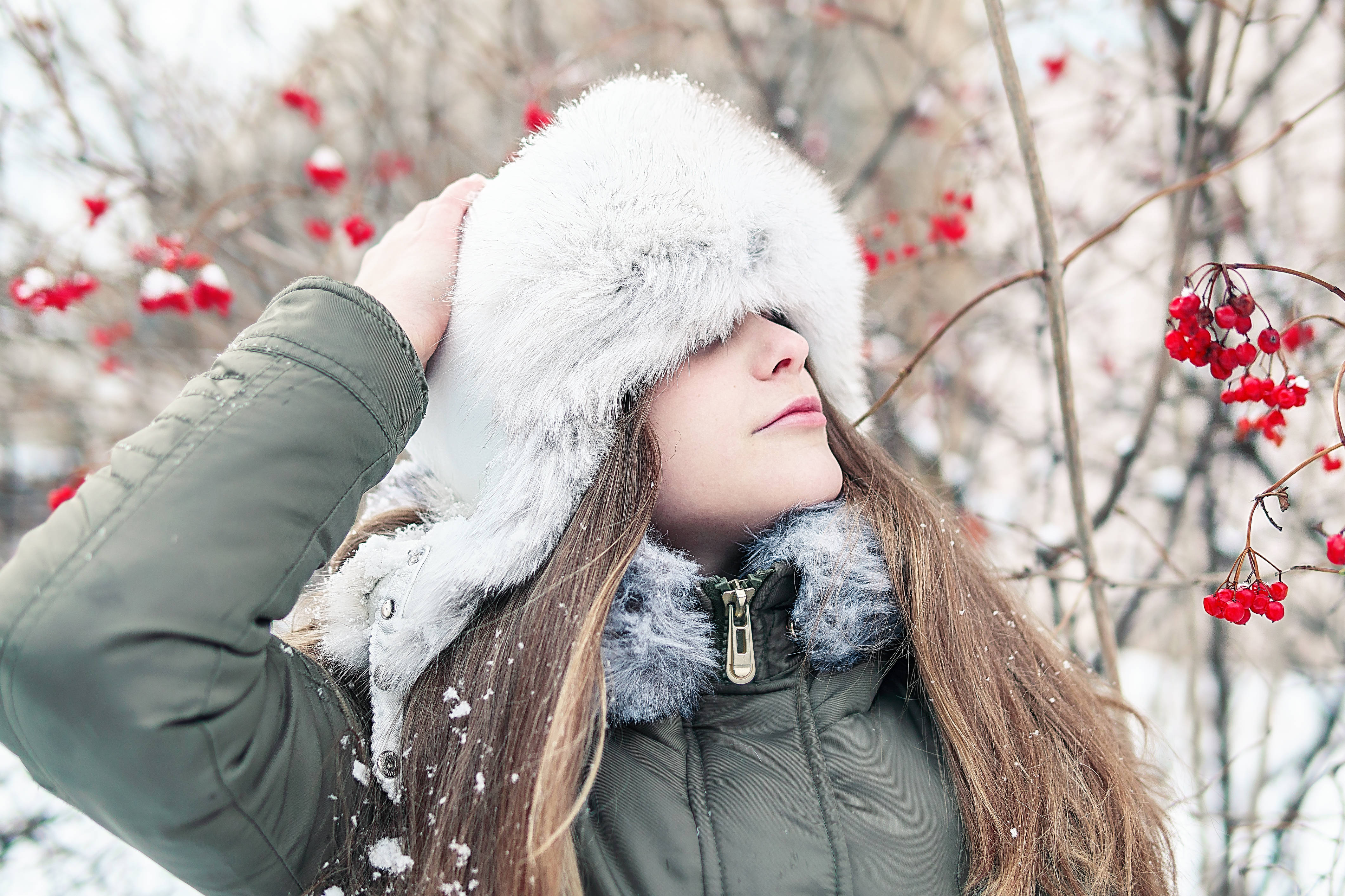 Pretty Christmas 桌布 壁紙 — 一位年輕女性戴著白色毛帽、穿著綠色外套，站在雪景中，周圍是光禿禿的樹枝上掛著紅色漿果。