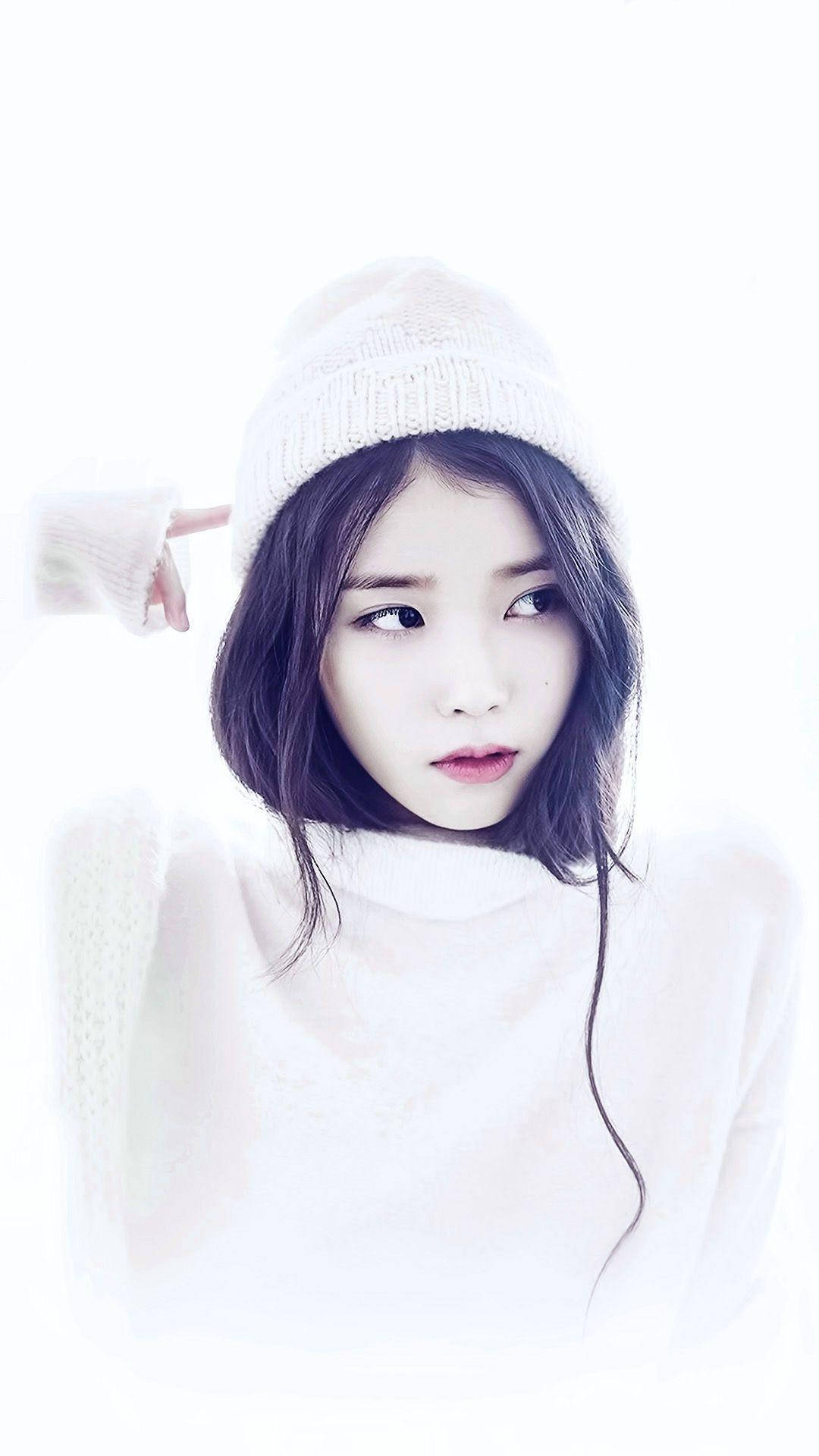 Kpop Aesthetic 桌布 壁紙 — 一位年輕女性戴著白色針織毛帽和穿著白色針織衫，在明亮的白色背景前側視，表情柔和。