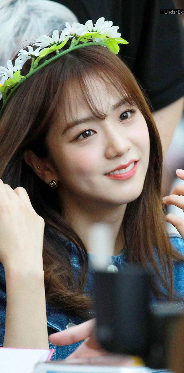 jisoo 可愛 桌布 壁紙 — 一位年輕女性戴著白色雛菊花冠，身穿牛仔上衣和金色耳環，溫暖地微笑。