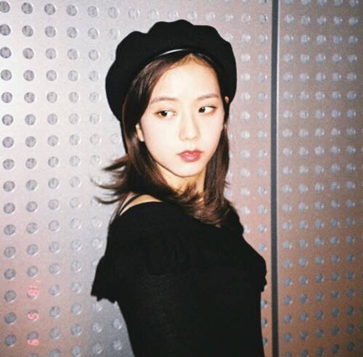 Jisoo Cute 桌布 壁紙 — 一位年輕女性戴著黑色貝雷帽和露肩上衣，在柔和的燈光下，靠著金屬穿孔牆擺姿勢。