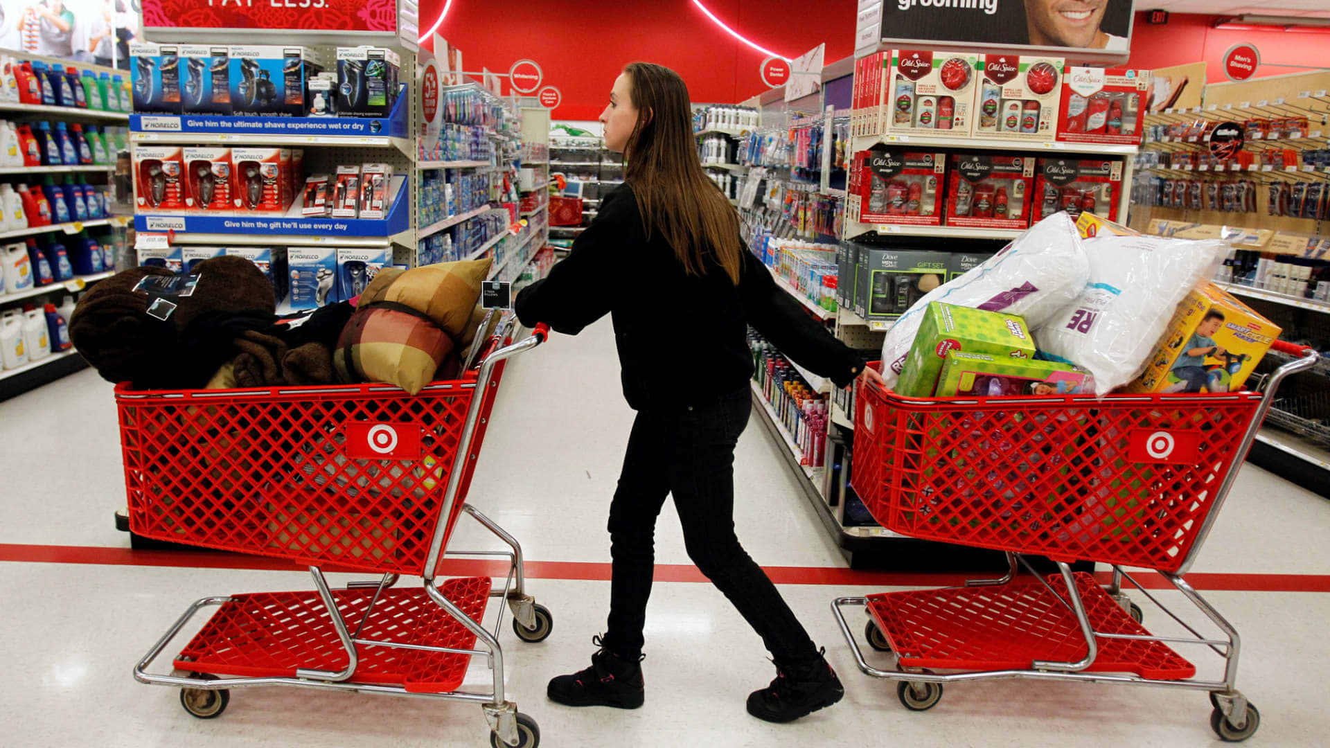 Shopping 桌布 壁紙 — 一位年輕女性推著兩輛裝滿物品的紅色Target購物車，穿過光線明亮的商店通道。