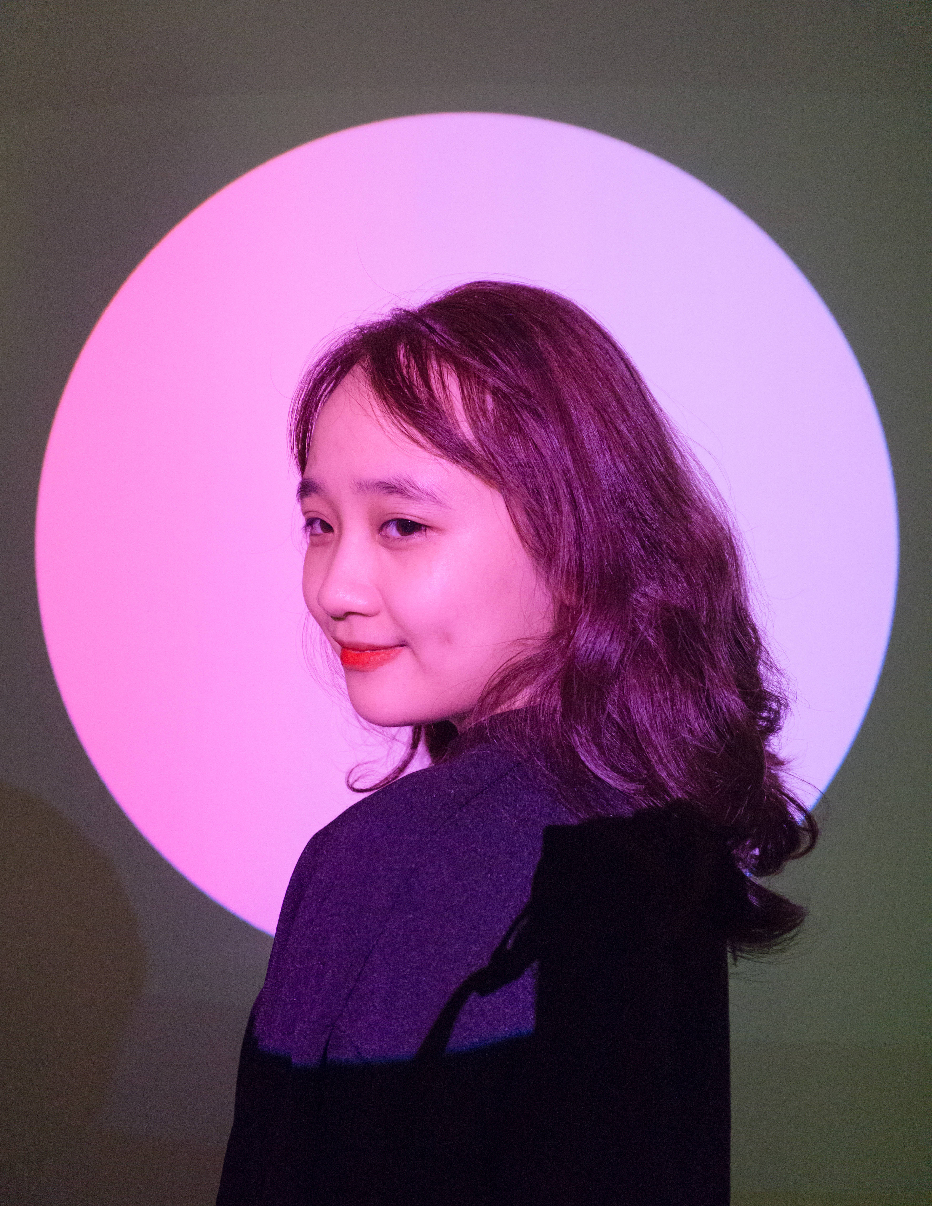 Cute Pink Girl 桌布 壁紙 — 一位年輕女性留著波浪長髮，在發光的粉紅色圓形背景前溫柔微笑。