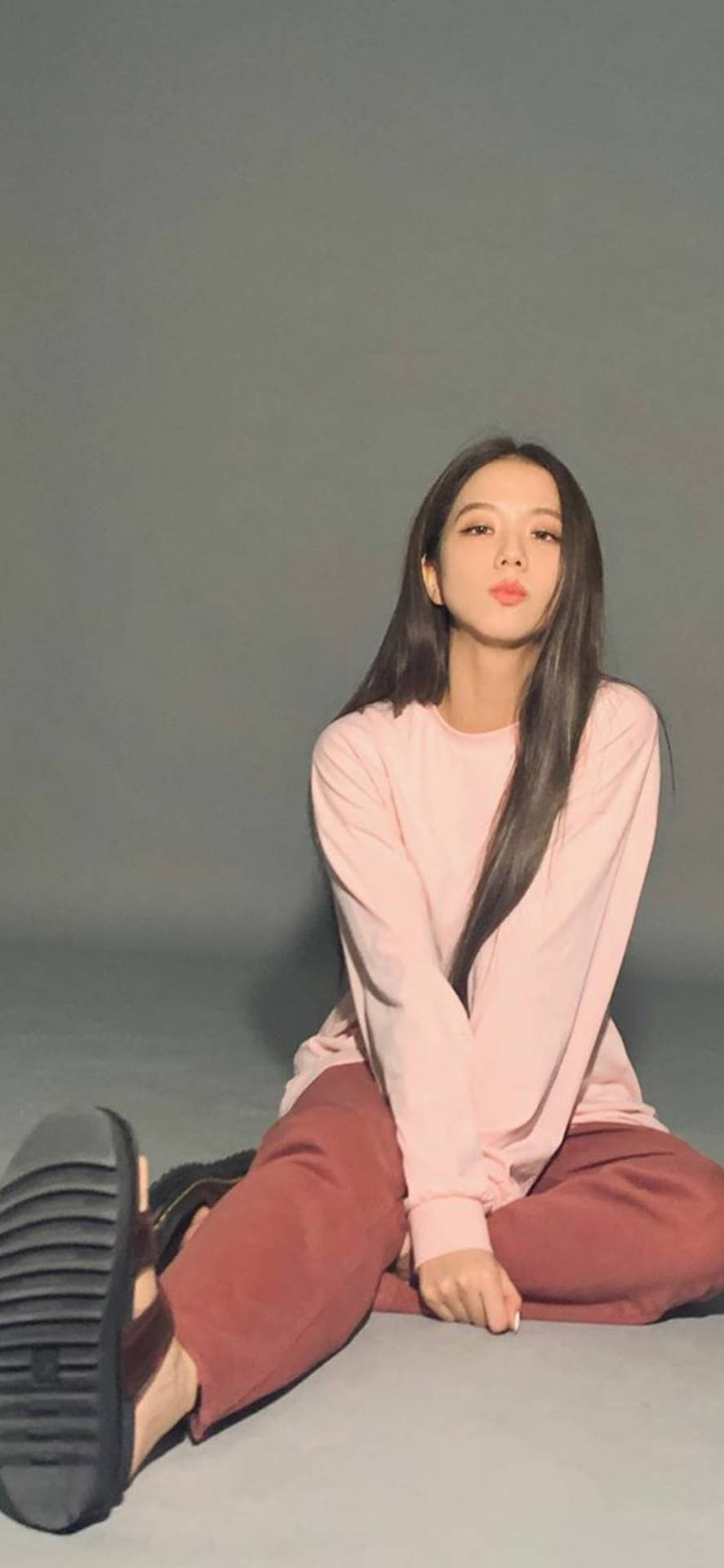 年輕女性盤腿坐在灰色地板上，身穿粉紅色上衣和栗色褲子。 — 智秀 GIF 壁紙