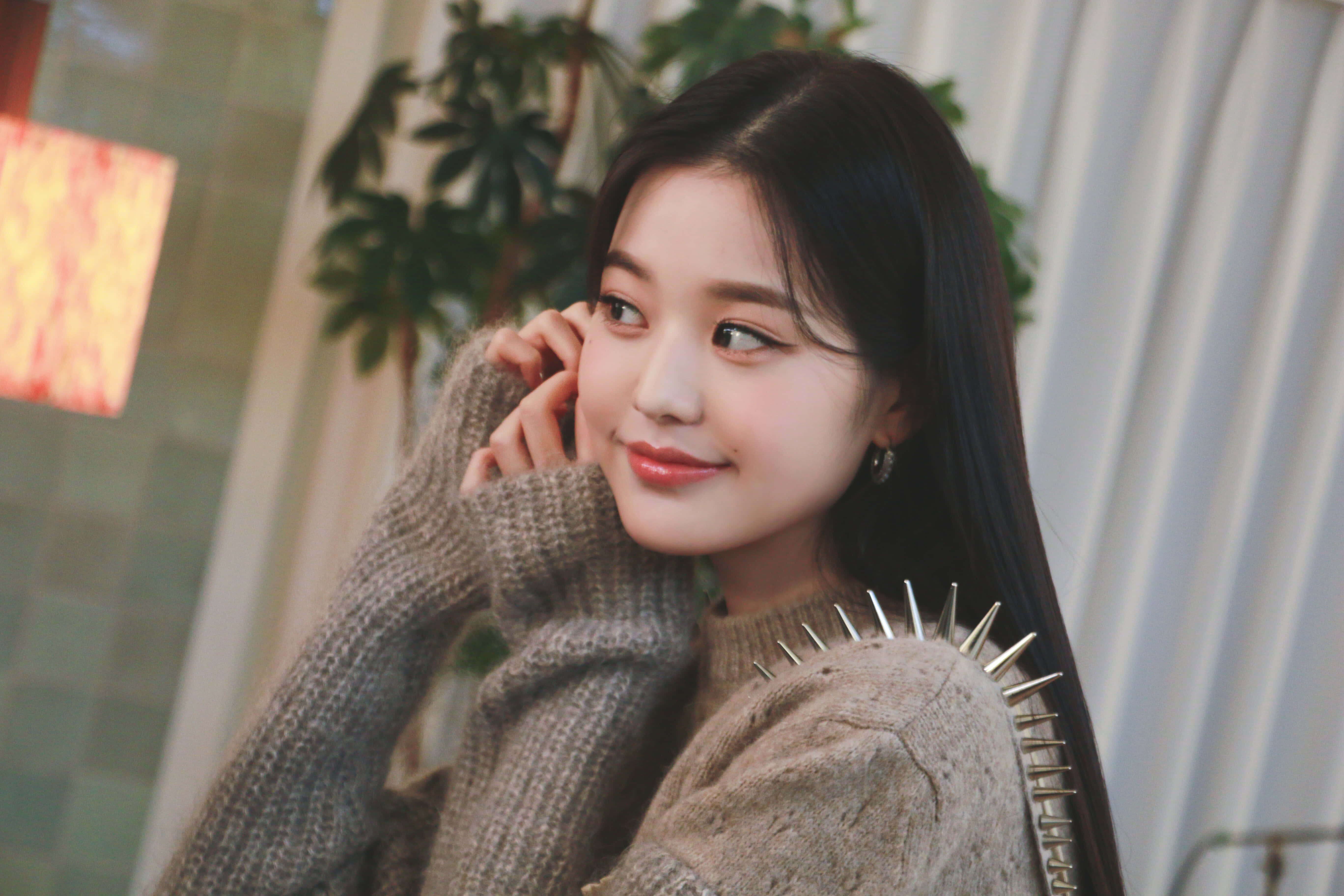 Pretty Girl Aesthetic 桌布 壁紙 — 一位年輕女性留著深色長髮，穿著一件質感灰色毛衣，肩上帶有銀色尖刺，溫柔地微笑。
