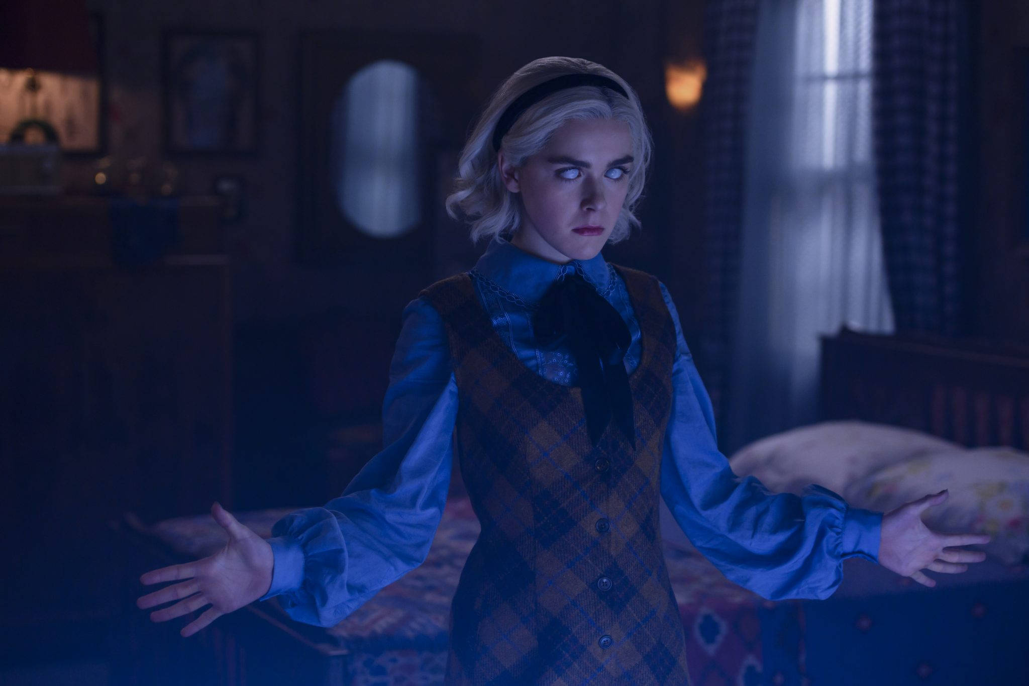 Kiernan Shipka 桌布 壁紙 — 一位年輕女性留著鉑金色頭髮，站在燈光昏暗的臥室中，雙臂伸展，身穿藍色襯衫和格子背心，在憂鬱的藍色燈光下。