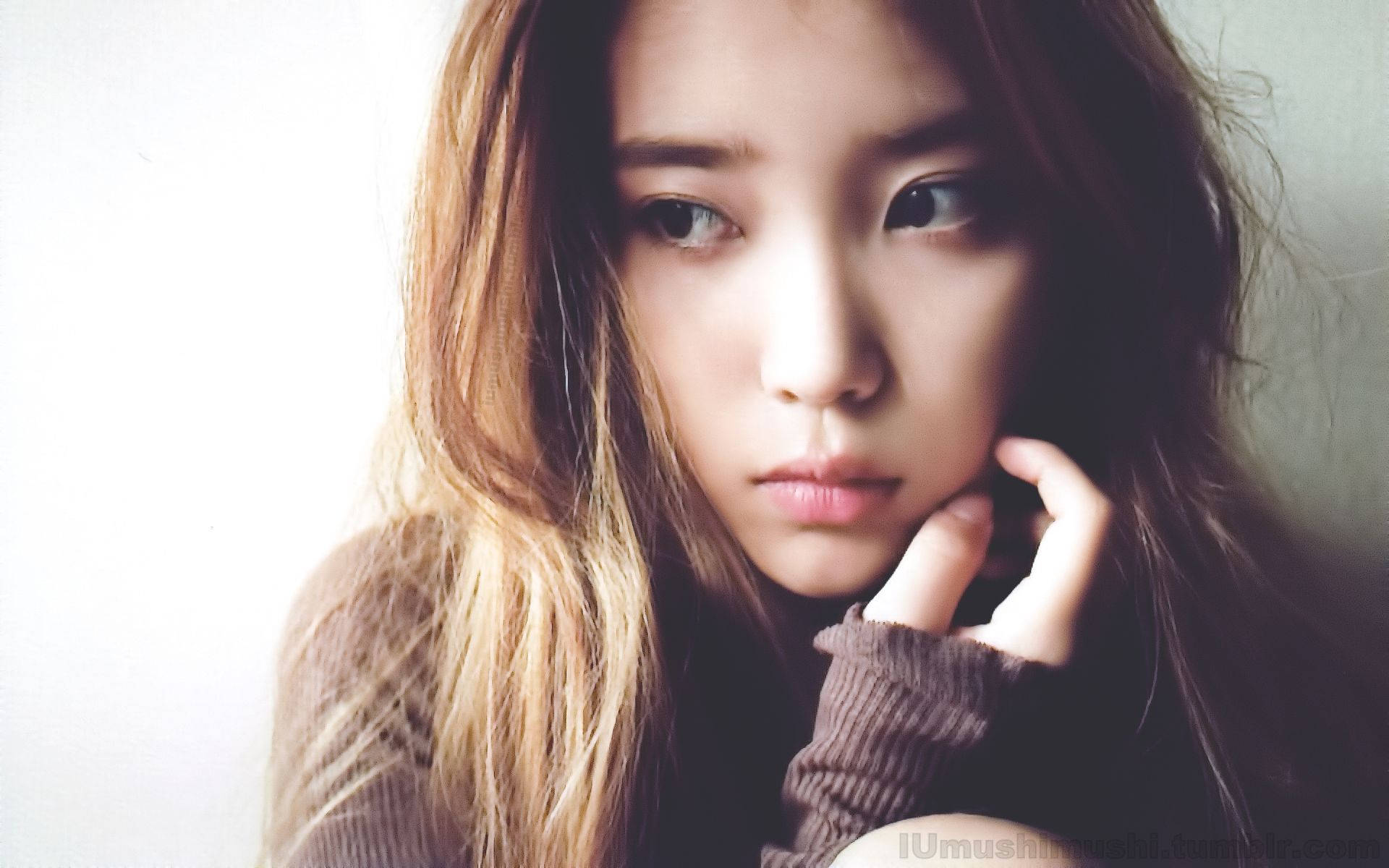 Kpop Aesthetic 桌布 壁紙 — 一位年輕女性留著長波浪髮，托腮凝視，背景是柔和的白色。