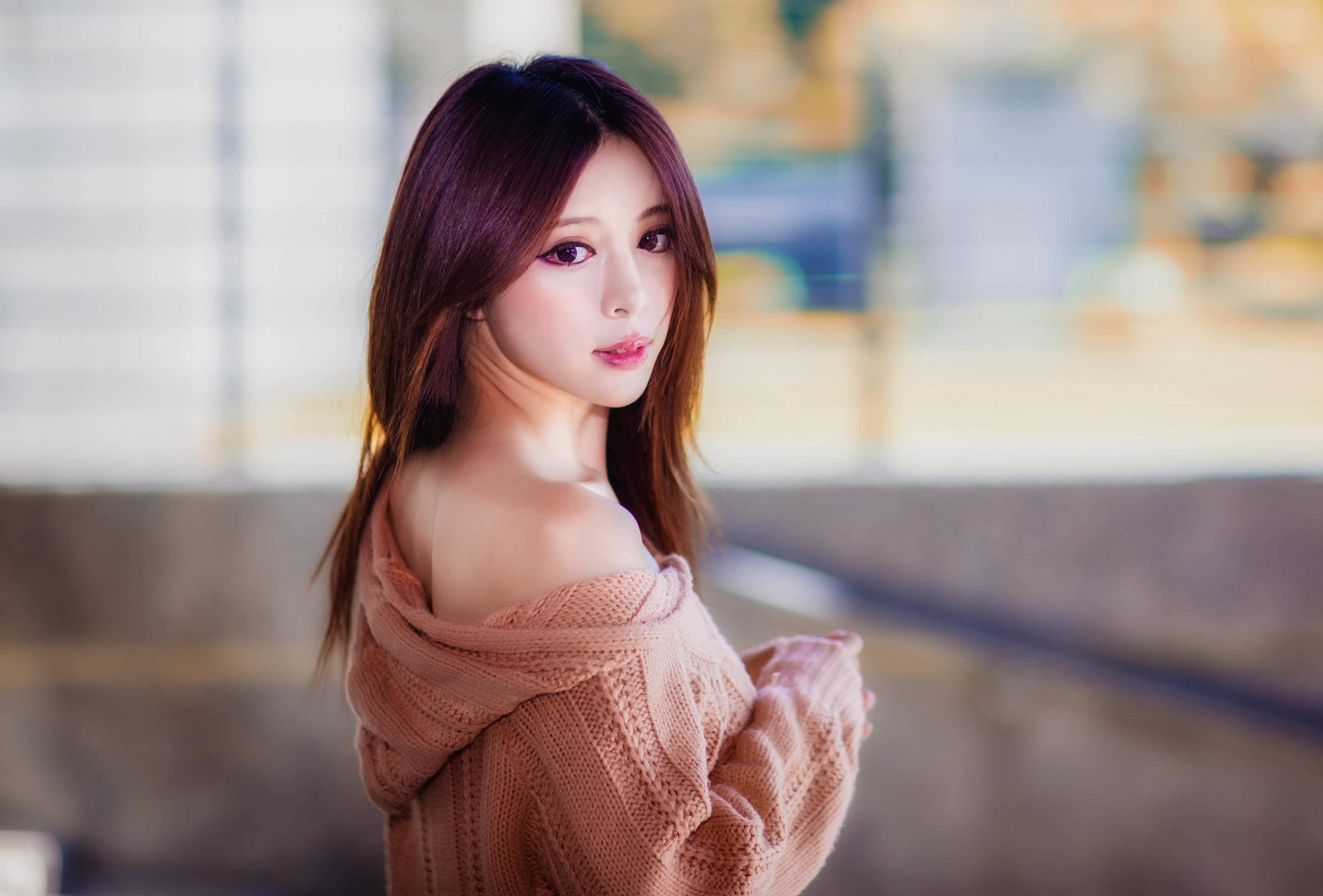 美女 桌布 壁紙 — 一位年輕女性留著長長的棕色頭髮，穿著柔軟的粉紅色針織毛衣，溫柔的表情越過肩膀回頭看。
