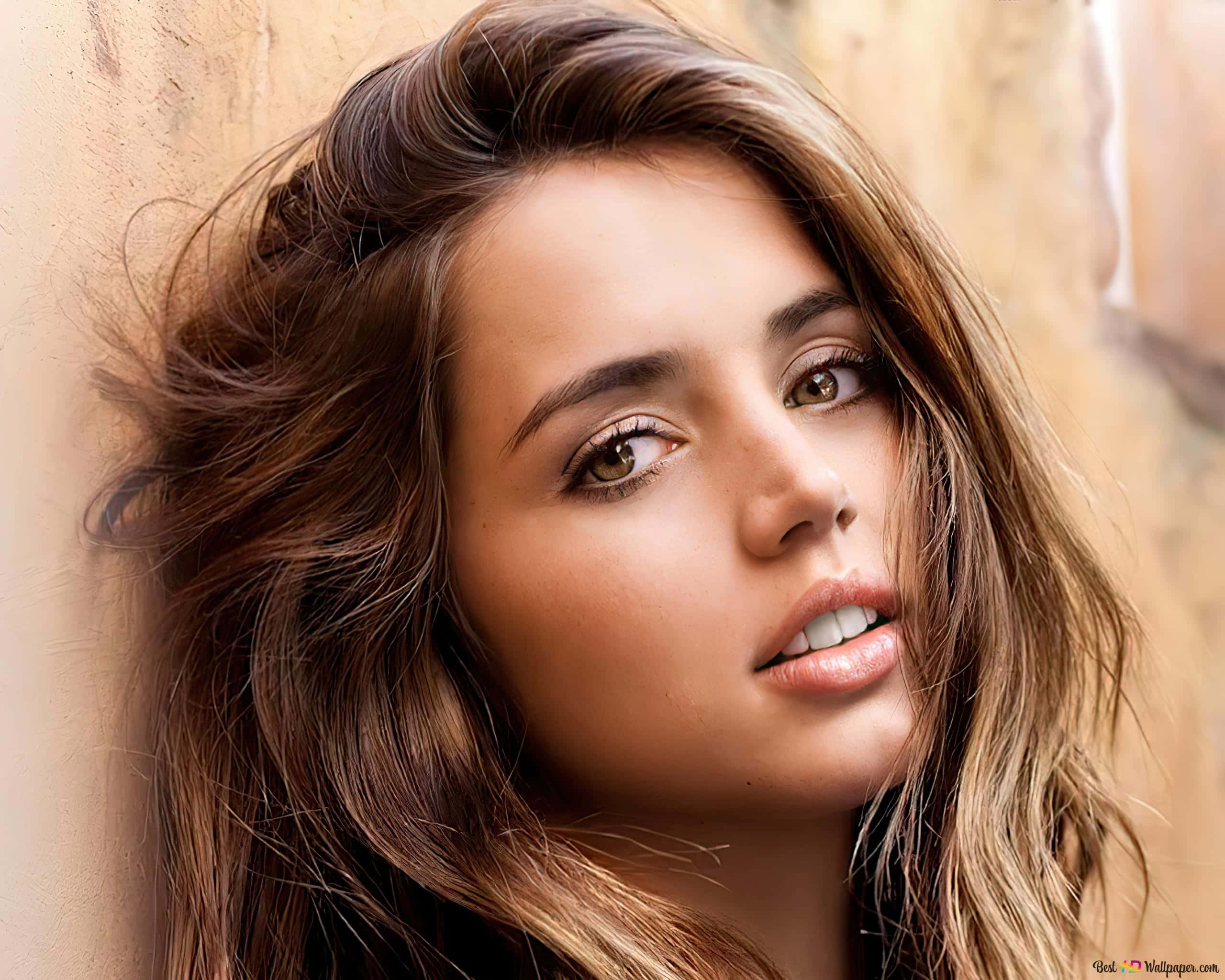 ana de armas 桌布 壁紙 — 一位年輕女性的特寫肖像，她有亂糟糟的棕色頭髮和溫暖的眼睛，靠在有紋理的米色牆上。