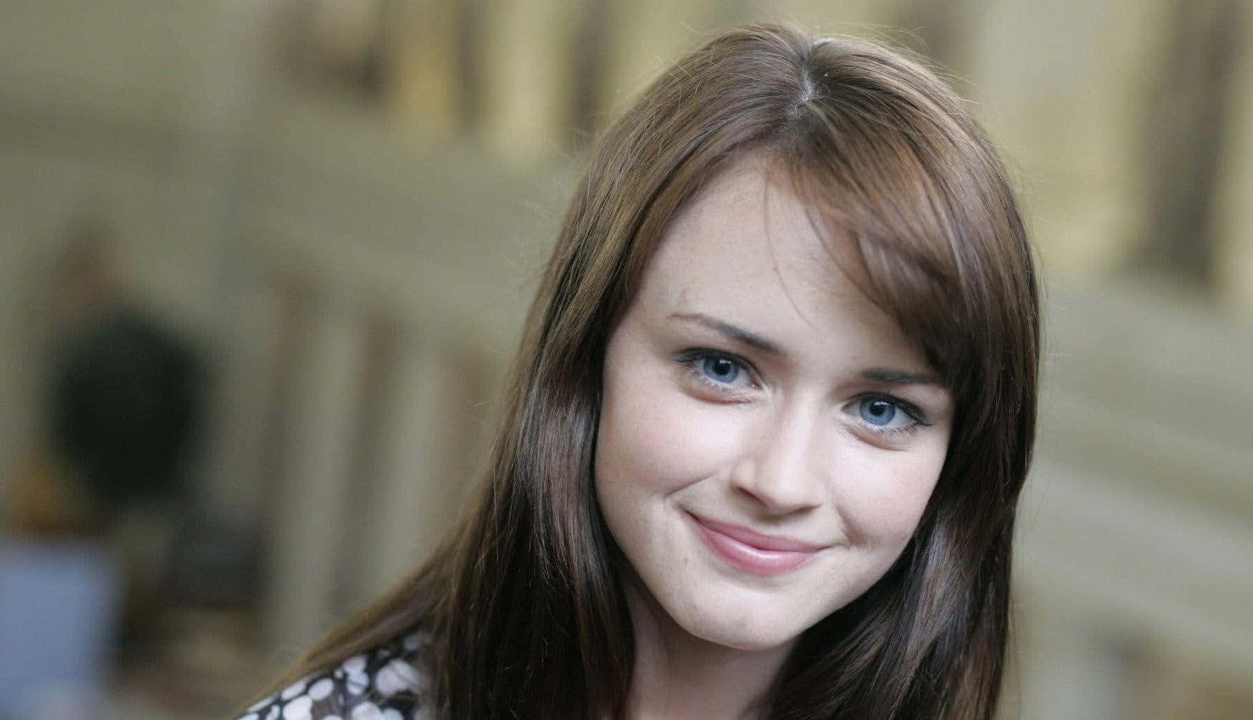 Alexis Bledel 桌布 壁紙 — 一位年輕女性的特寫肖像，她有棕色頭髮和藍色眼睛，正溫暖地對著鏡頭微笑。