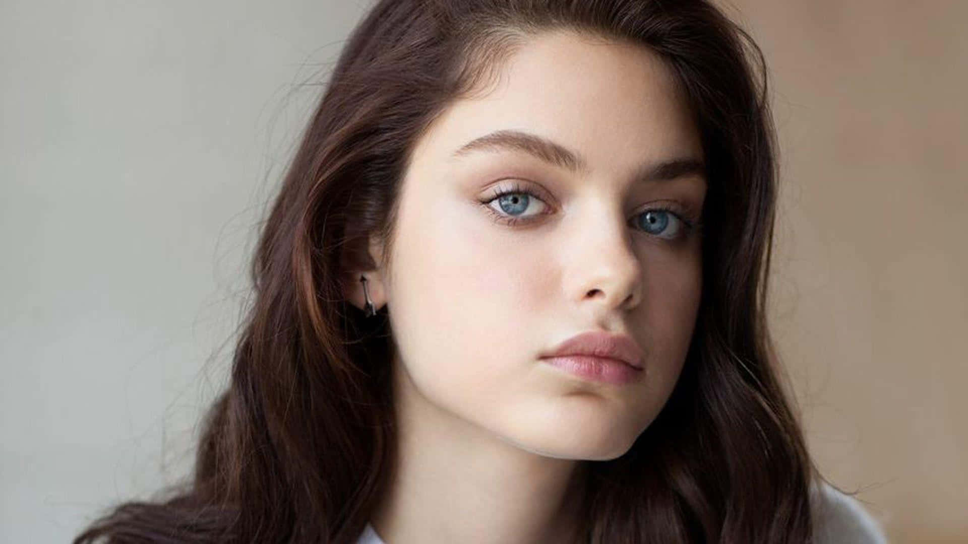 Odeya Rush 桌布 壁紙 — 一位年輕女性的特寫肖像，擁有引人注目的藍色眼睛和長長的棕色頭髮，直視鏡頭。