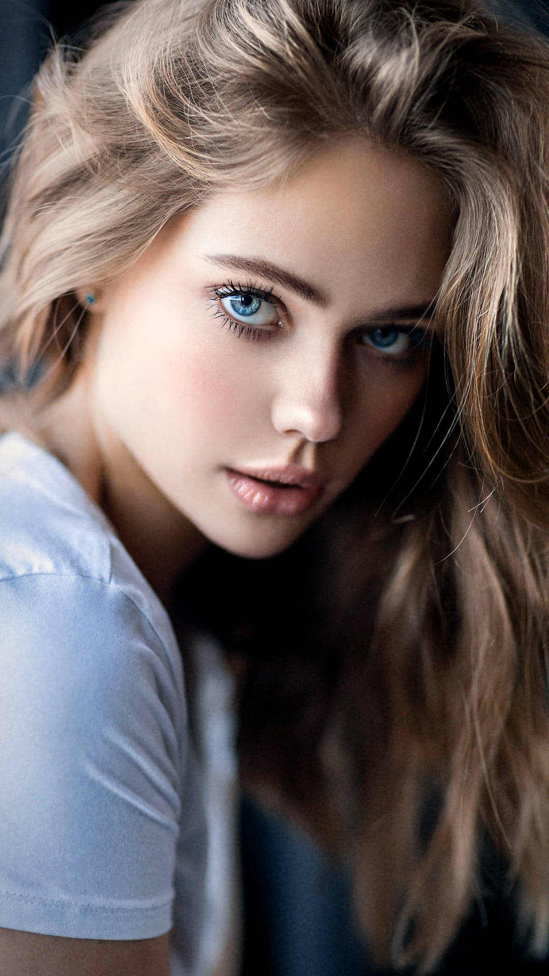 Beautiful Woman 桌布 壁紙 — 一位年輕女性的特寫肖像，擁有引人注目的藍色眼睛和波浪金髮，身穿淺藍色T恤。