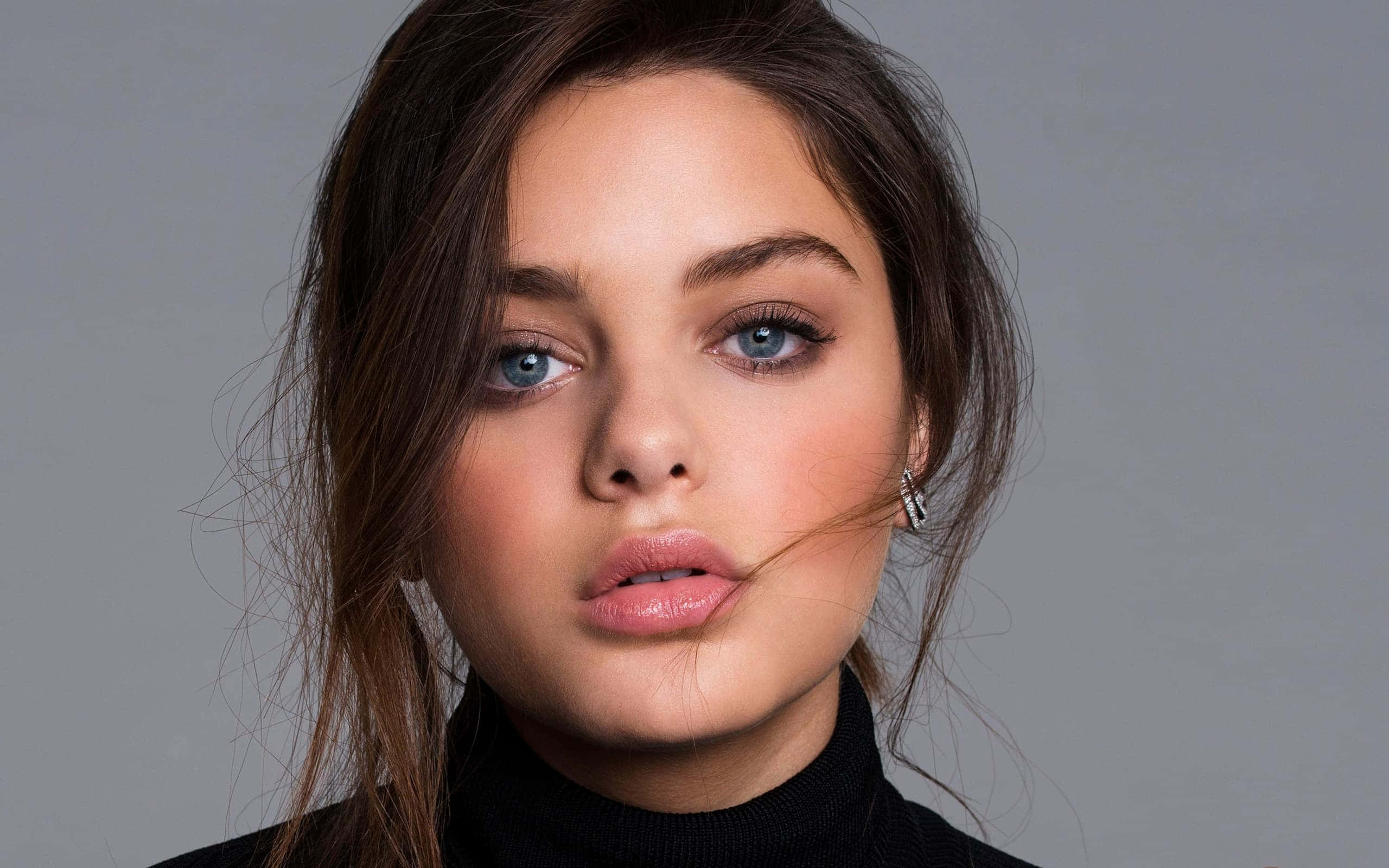 Odeya Rush 桌布 壁紙 — 一位年輕女性的特寫肖像，擁有引人注目的藍色眼睛和深色頭髮，背景為中性灰色。