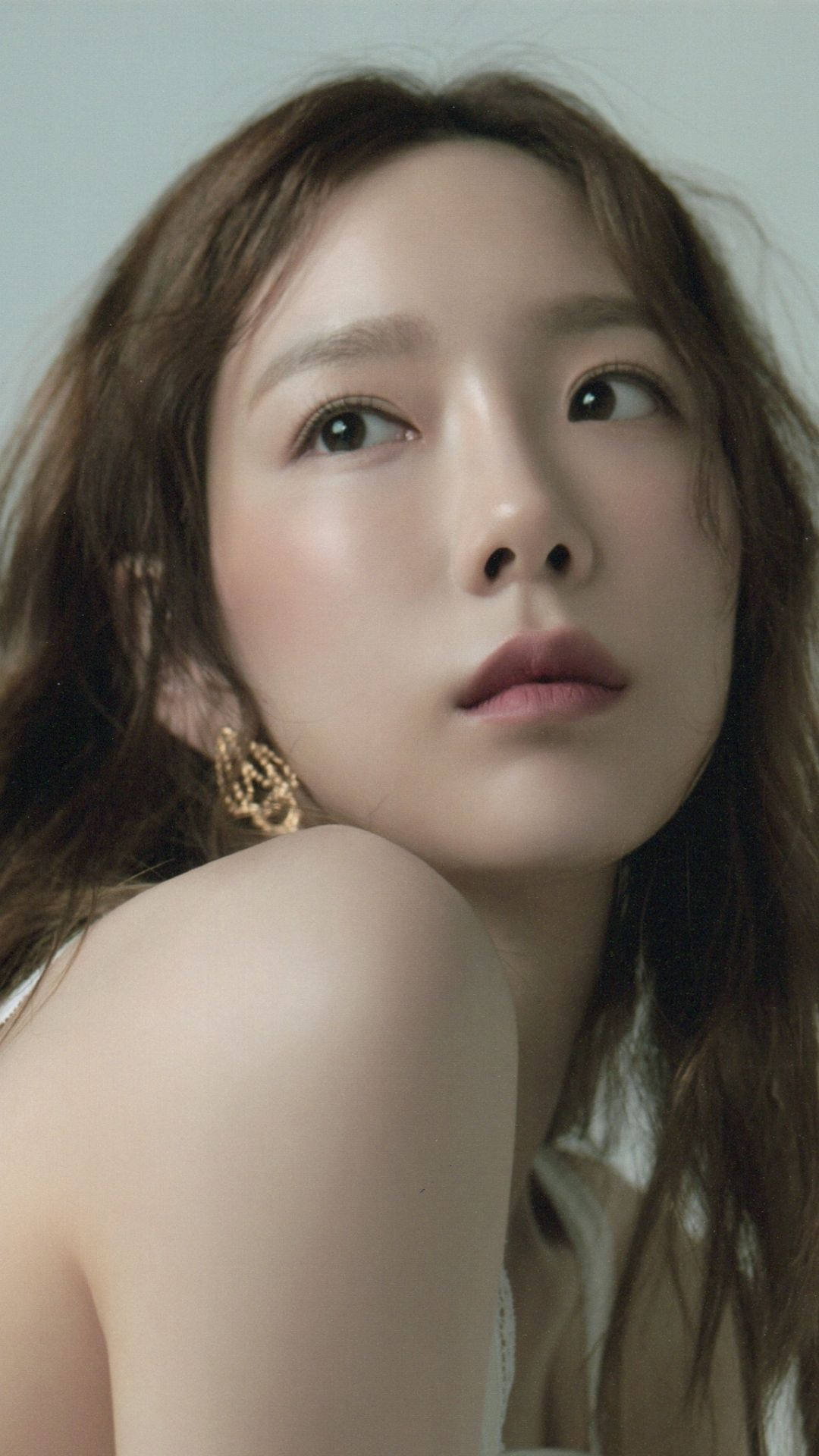 태연 桌布 壁紙 — 一位年輕女性的特寫肖像，擁有柔軟的棕色頭髮和金色耳環，帶著沉思的表情向上凝視。