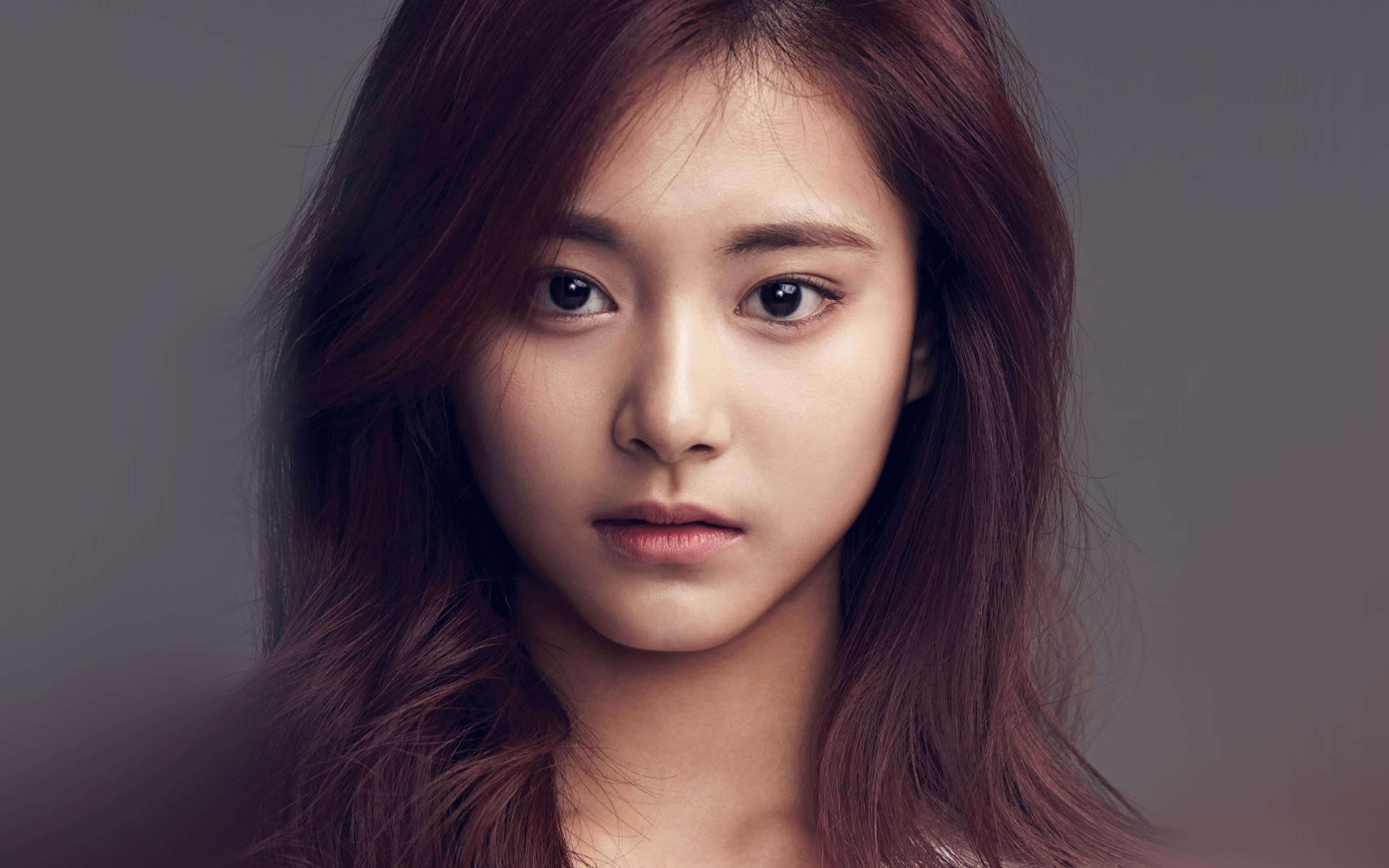 twice 桌布 壁紙 — 一位年輕女性的特寫肖像，擁有長長的紅褐色頭髮和強烈的凝視，背景是柔和的灰色。