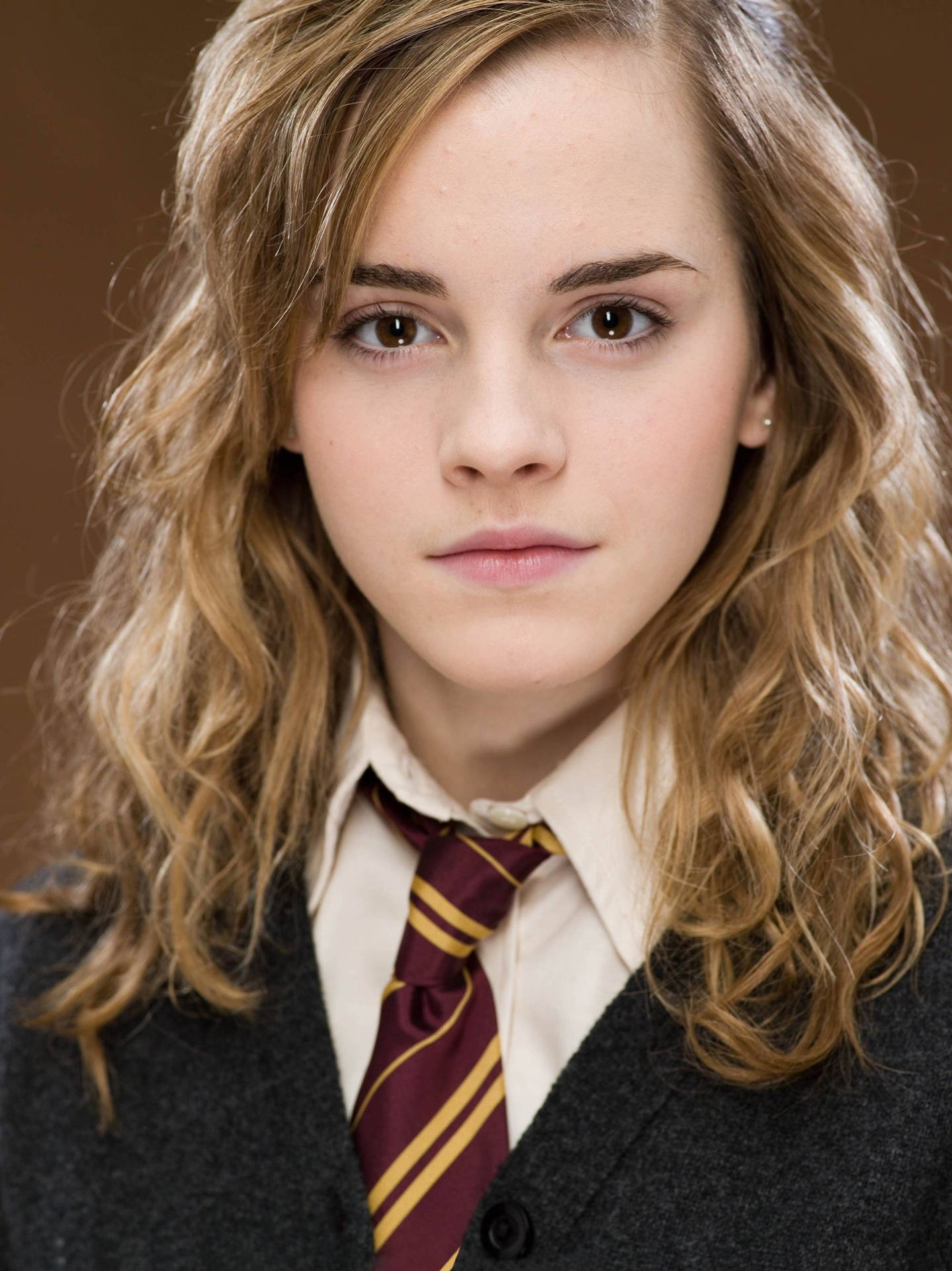 Hermione Granger 桌布 壁紙 — 一位年輕女性的特寫肖像，波浪形金髮，穿著帶有栗色和金色條紋領帶的校服。