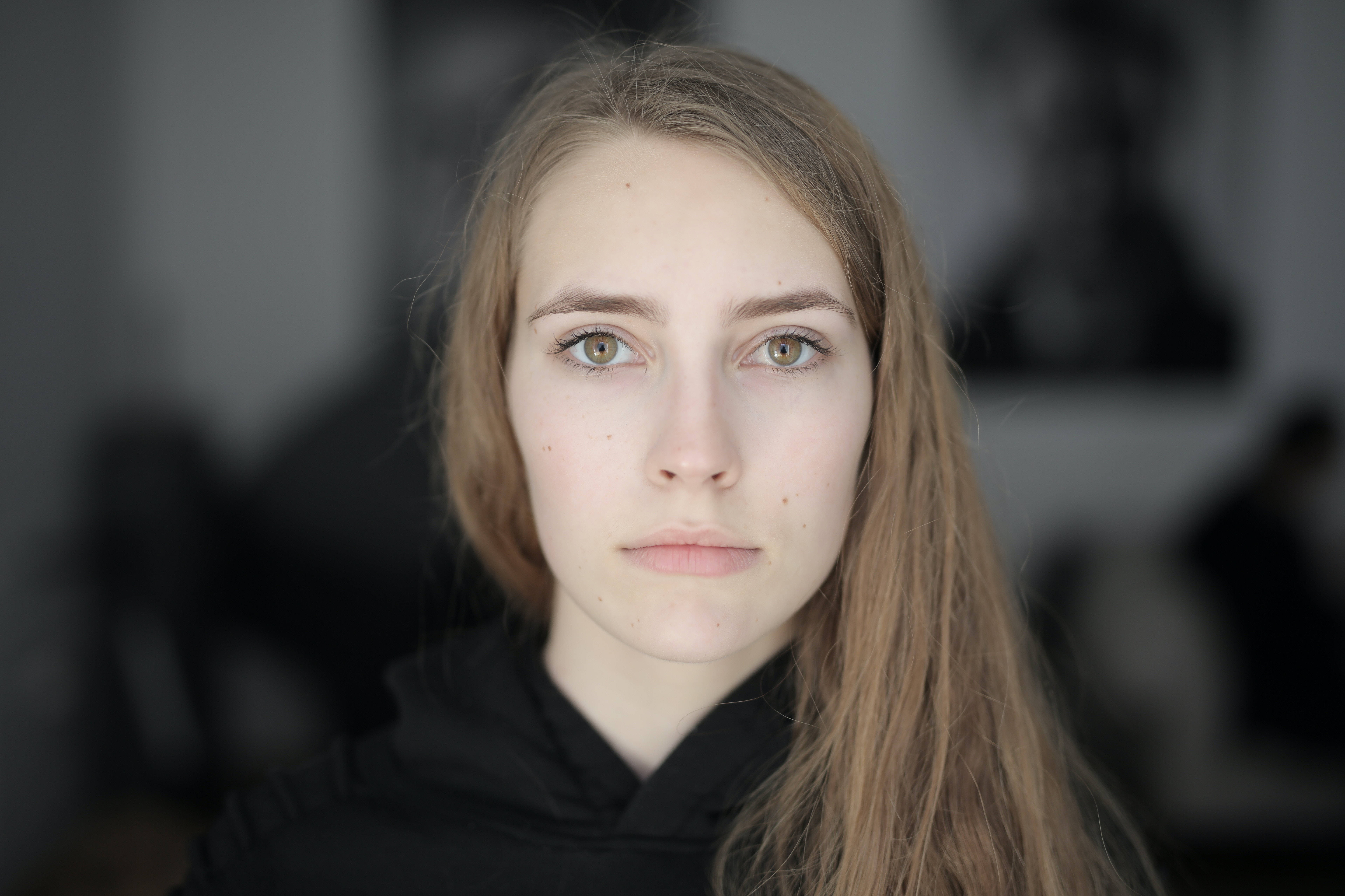headshot 桌布 壁紙 — 一位年輕女性的特寫肖像，長長的棕色頭髮和綠色眼睛，直視相機，背景是柔和模糊的室內環境。