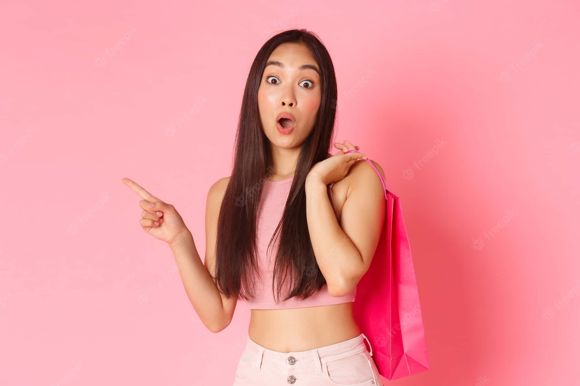 Teenage 桌布 壁紙 — 一位年輕女性睜大眼睛、張開嘴巴，興奮地指著一個粉紅色購物袋，背景為純粉紅色。