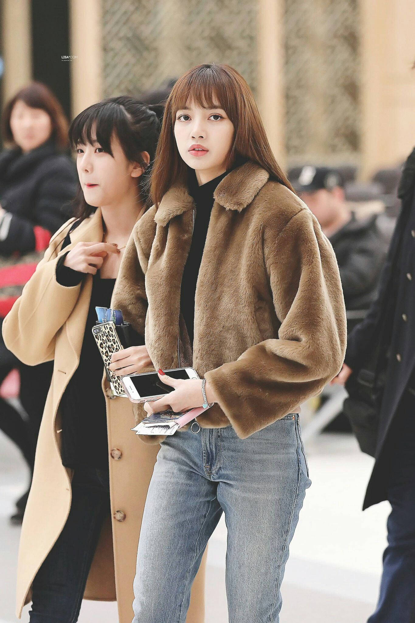 Lalisa 桌布 壁紙 — 一位年輕女性穿著棕色人造毛皮外套和牛仔褲，自信地站在繁忙的城市人群中，手持手機和錢包。