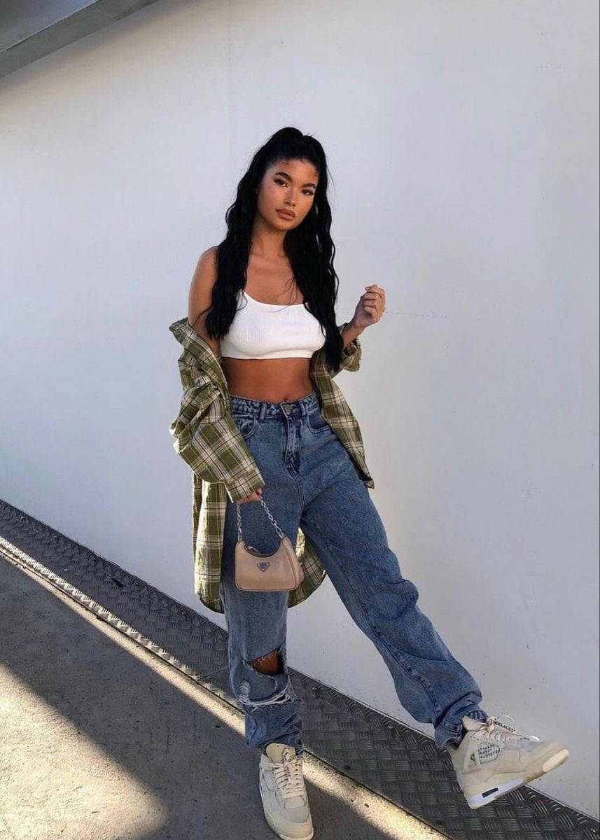 Denim 桌布 壁紙 — 一位年輕女性穿著破洞牛仔褲和格紋襯衫，在明亮的日光下靠著白色牆壁。