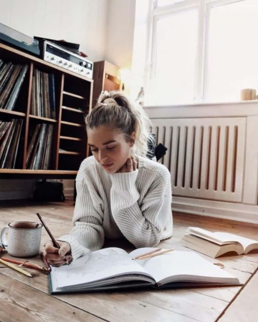 Study Aesthetic 桌布 壁紙 — 一位年輕女性穿著舒適的白色毛衣，在木地板上畫素描本，旁邊放著馬克杯和黑膠唱片。