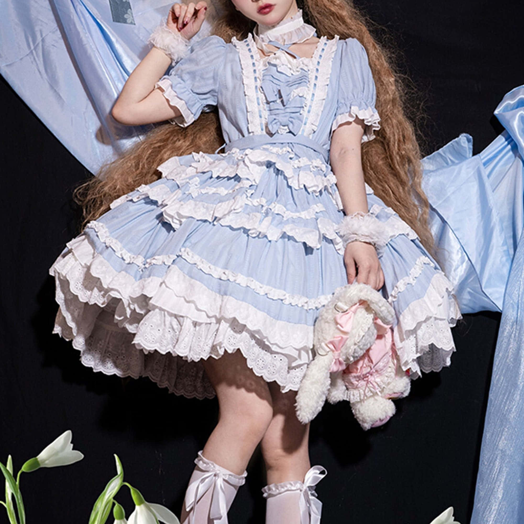 Lolita Fashion 桌布 壁紙 — 一位年輕女性穿著蓬鬆的淺藍色和白色荷葉邊洛麗塔連衣裙，在黑暗背景襯托白色花朵前，抱著毛絨玩具擺姿勢。