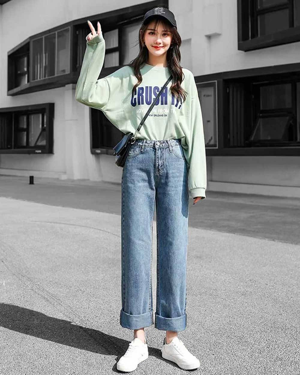 Denim 桌布 壁紙 — 一位年輕女性穿著薄荷綠運動衫和捲起褲管的牛仔褲，在明亮的日光下於城市人行道上愉快地擺姿勢。