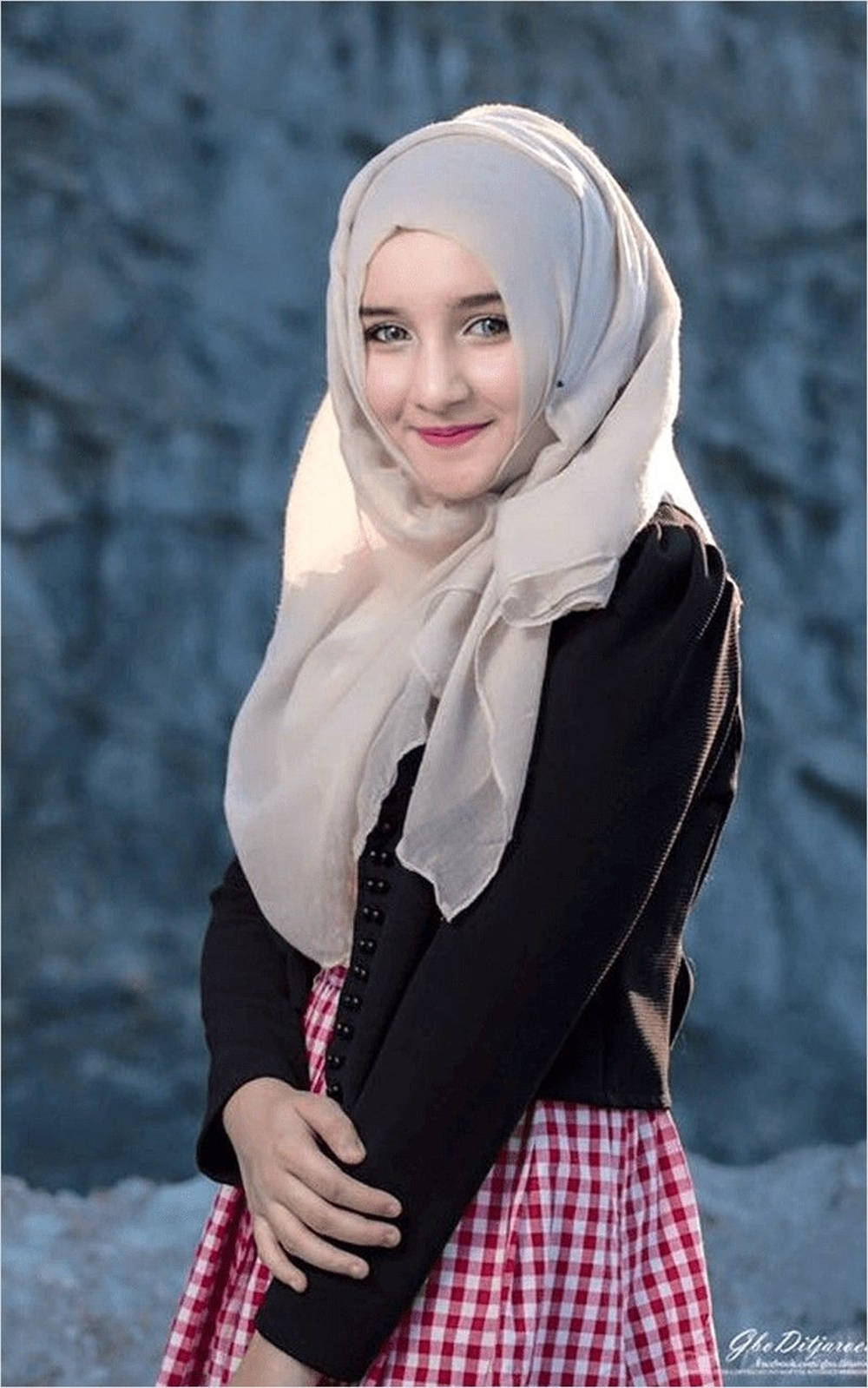 muslim 桌布 壁紙 — 一位年輕女性穿著輕薄頭巾和紅色格紋裙，在紋理藍色石牆前溫暖微笑。