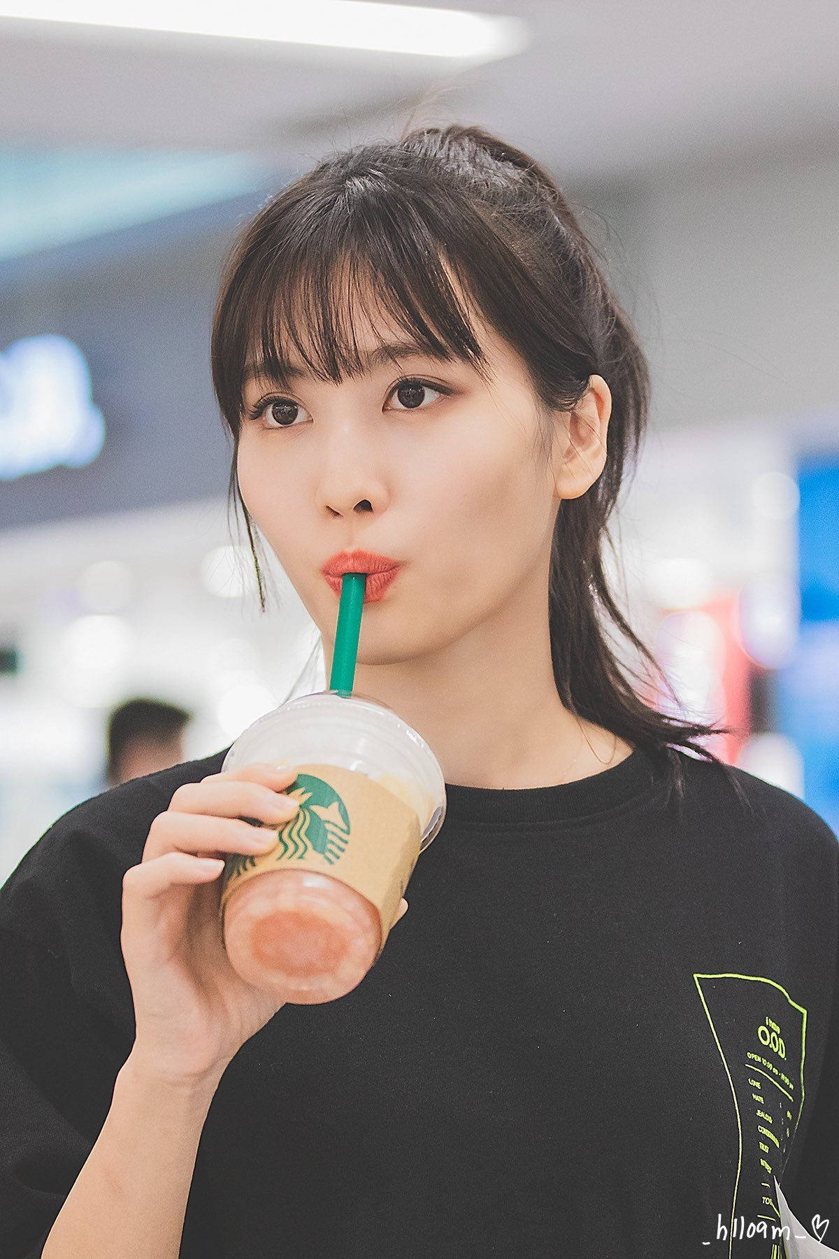 Momo 桌布 壁紙 — 一位年輕女性穿著黑色T恤，在明亮的室內環境中用綠色吸管啜飲粉紅色的星巴克飲料。