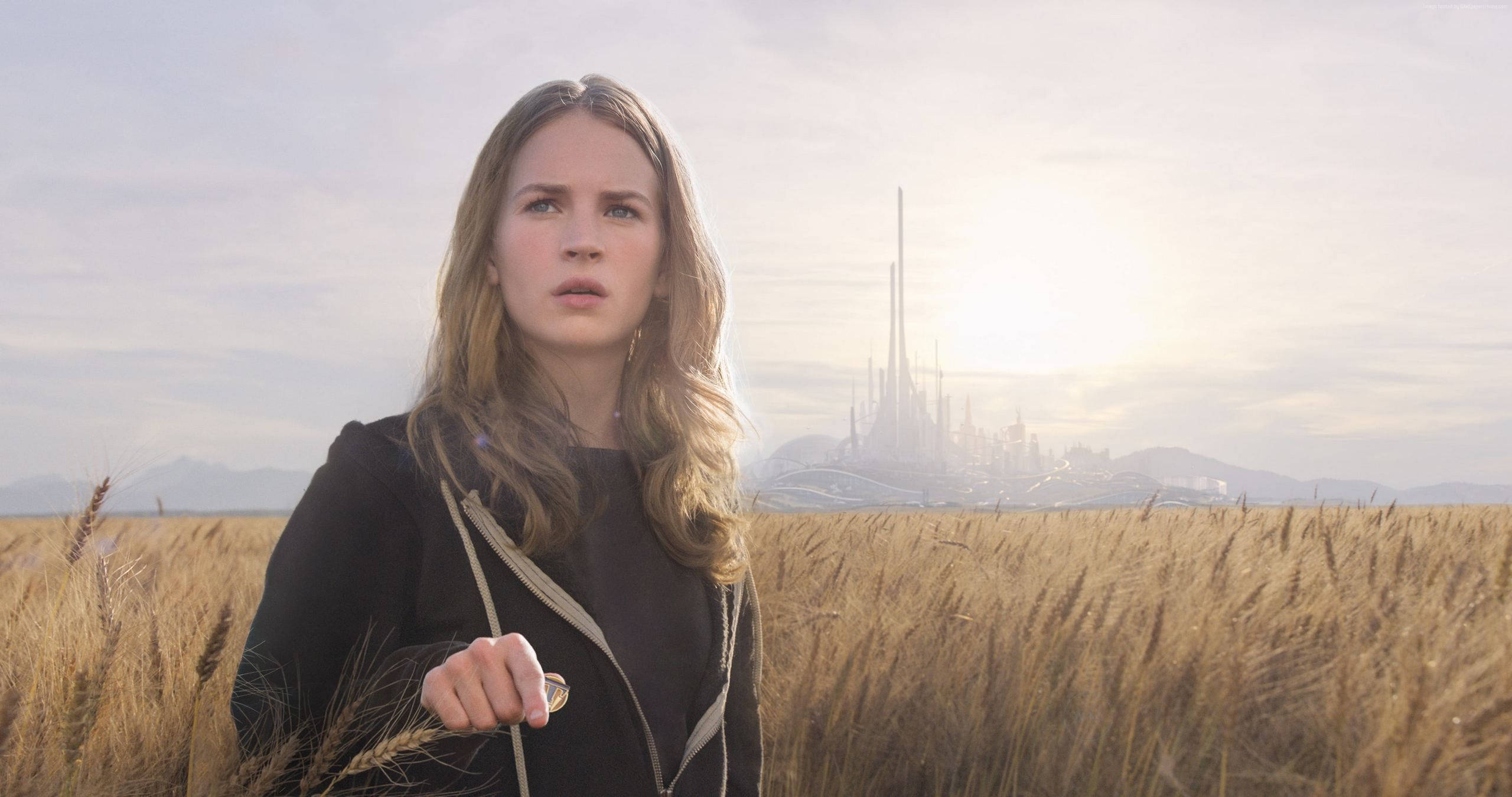 Tomorrowland Movie 桌布 壁紙 — 一位年輕女性站在金色麥田裡，凝視著遠方在朦朧日出下閃耀的未來城市。
