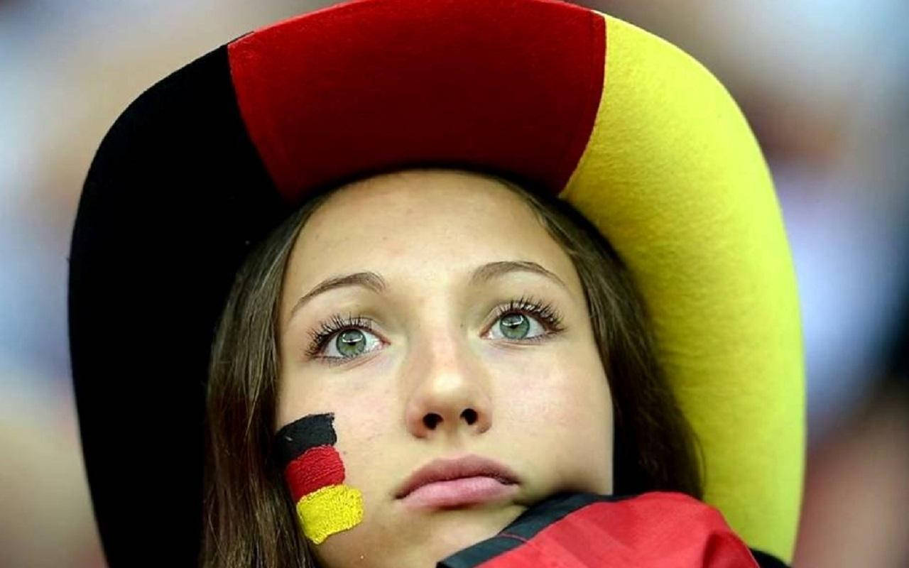 German Girl 桌布 壁紙 — 一位年輕女性臉頰上畫有德國國旗，戴著三色帽，專注地向上凝視。