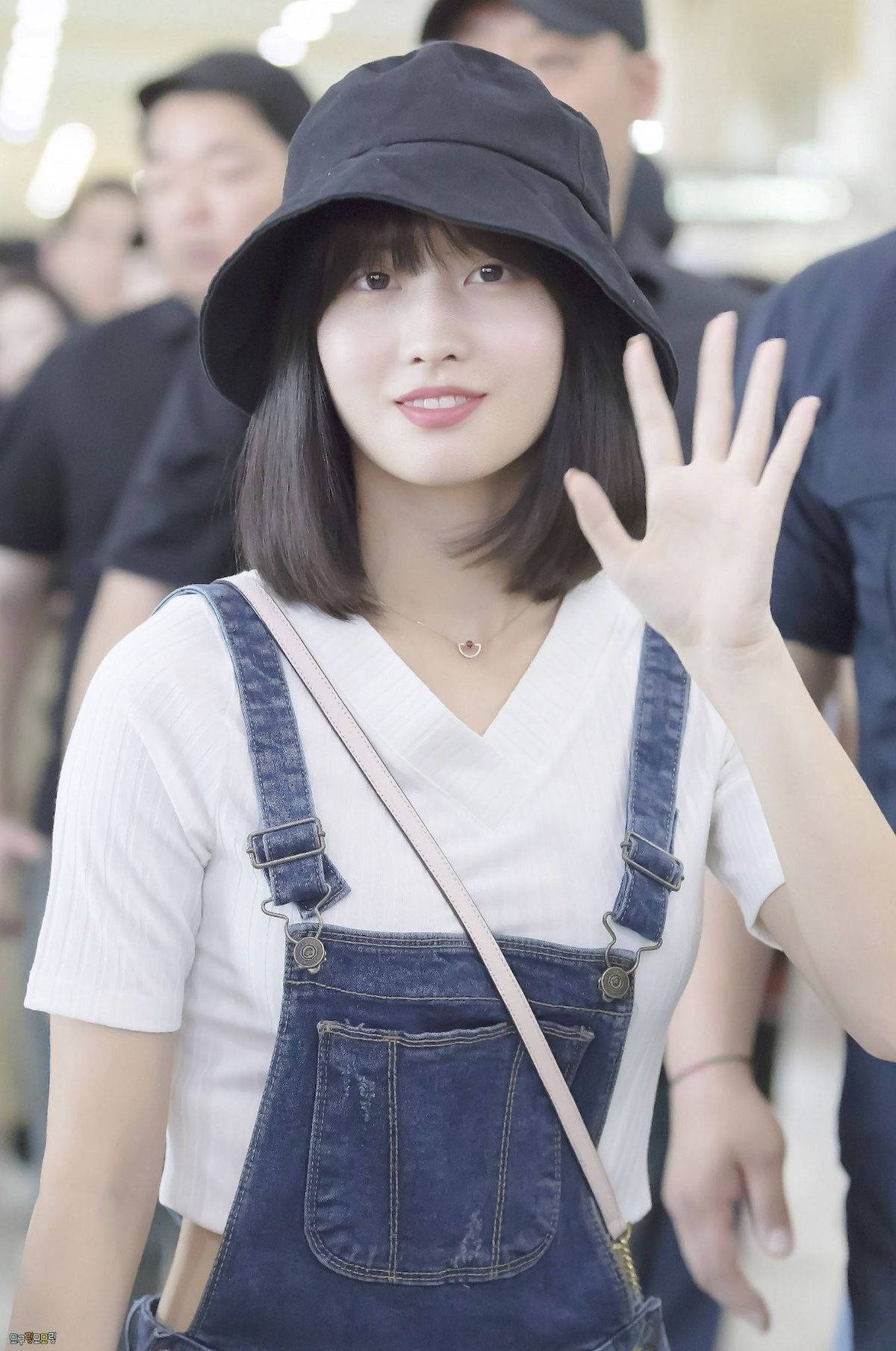 Momo 桌布 壁紙 — 一位年輕女性身穿牛仔工裝褲和黑色漁夫帽，在明亮的室內環境中愉快地向鏡頭揮手。