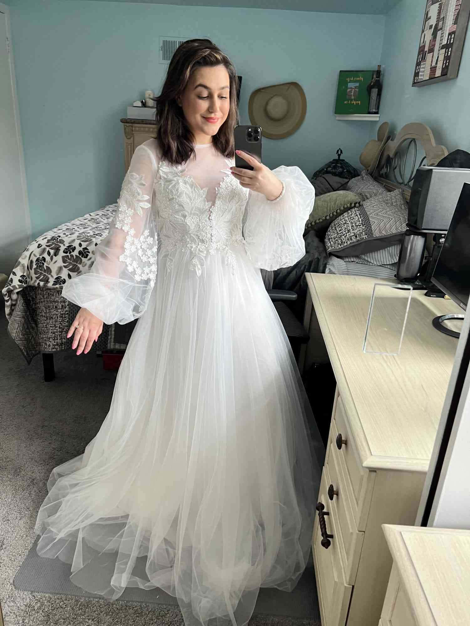 Bride's Dress 桌布 壁紙 — 一位年輕女性身穿白色薄紗婚紗，搭配蕾絲袖，在臥室對著鏡子自拍。