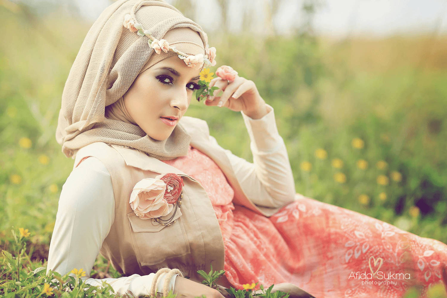 muslim 桌布 壁紙 — 一位年輕女性身穿米色頭巾，頭巾上飾有花朵，躺在陽光明媚、點綴著黃色花朵的草地上。