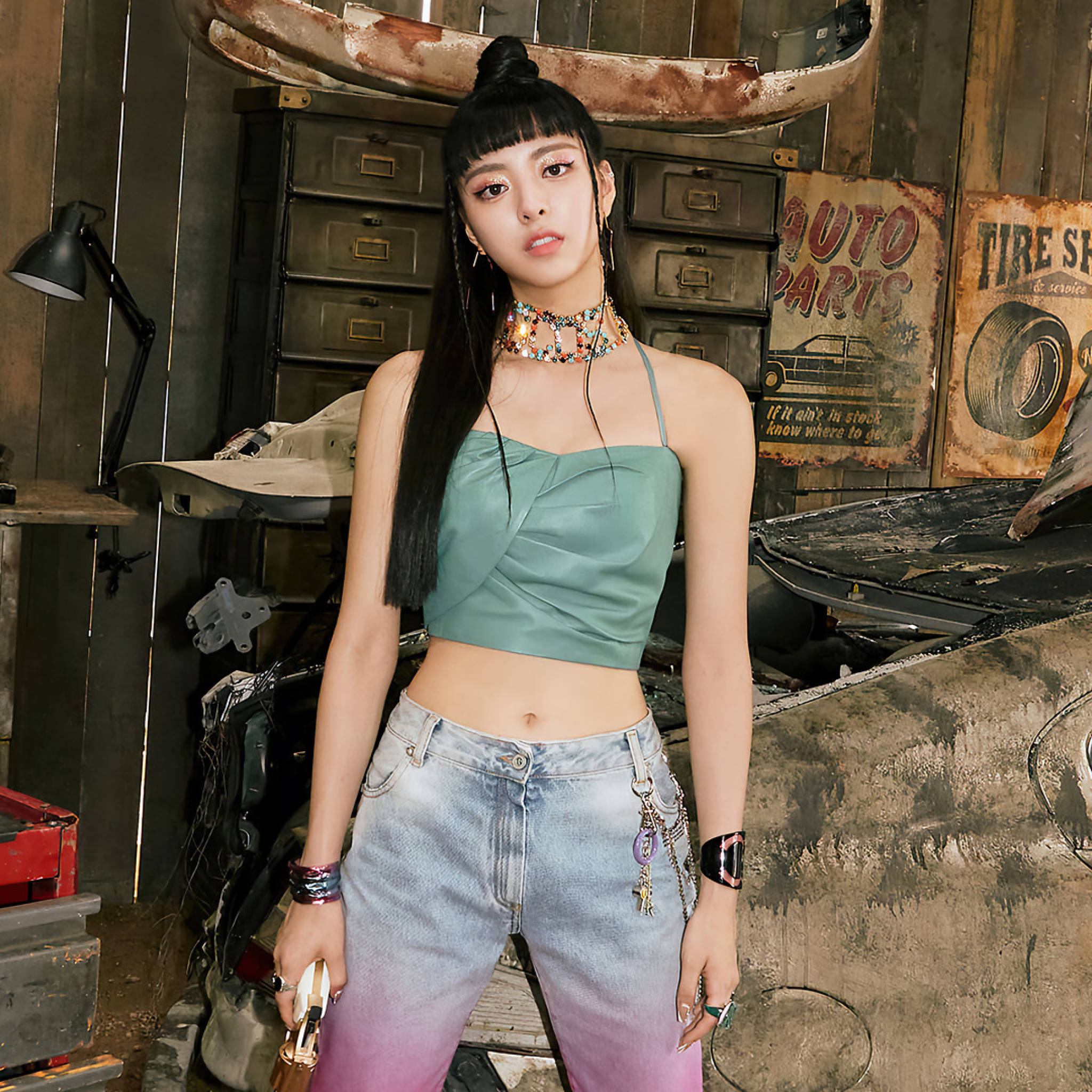 ITZY 桌布 壁紙 — 一位年輕女性身穿綠色短版上衣和漸變牛仔褲，在充滿復古標誌和工具的鄉村風格汽車修理廠自信地擺姿勢。
