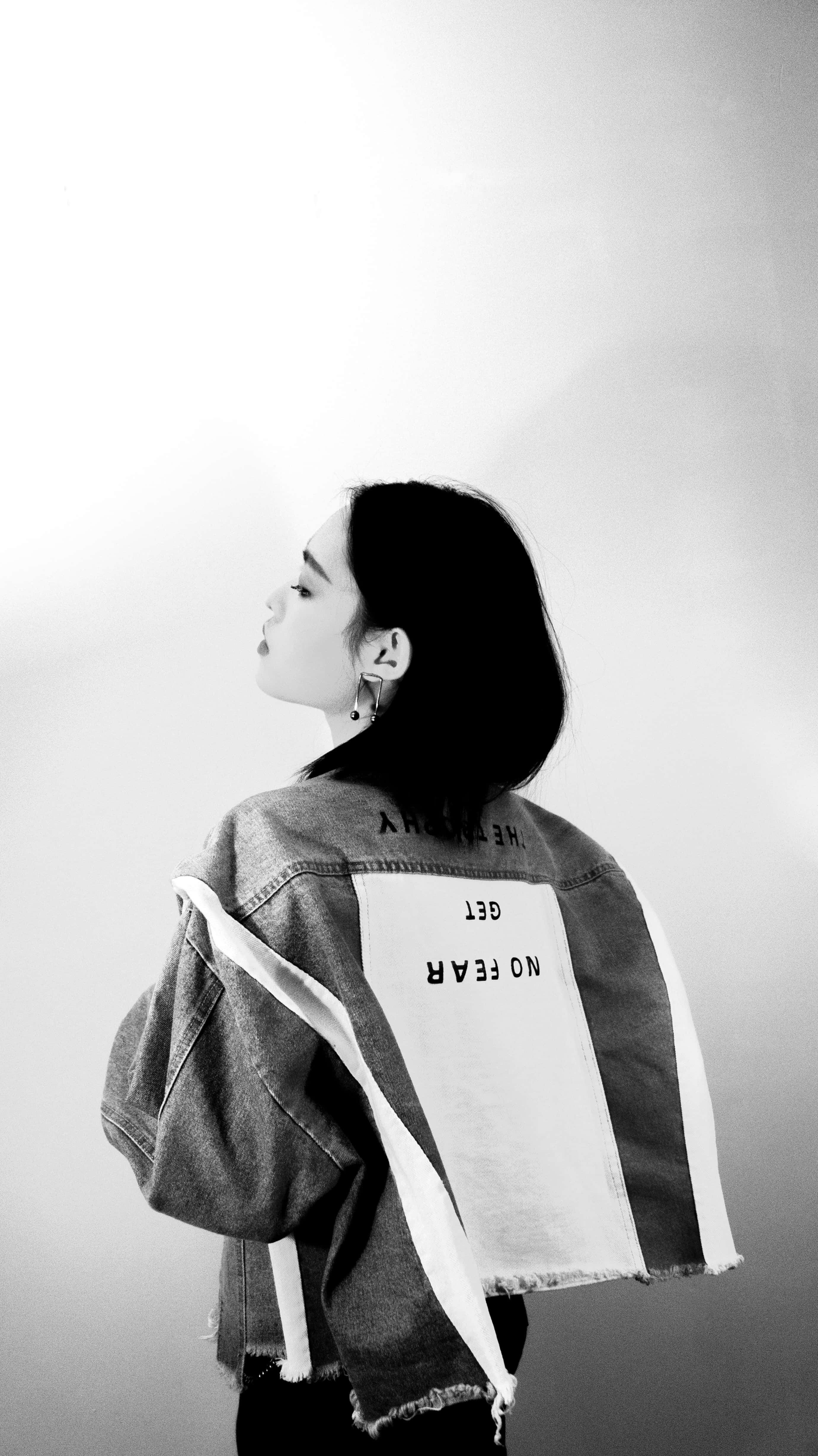 Black And White Fashion 桌布 壁紙 — 一位年輕女性身穿背後印有粗體文字的牛仔外套，側身站在素色背景前。