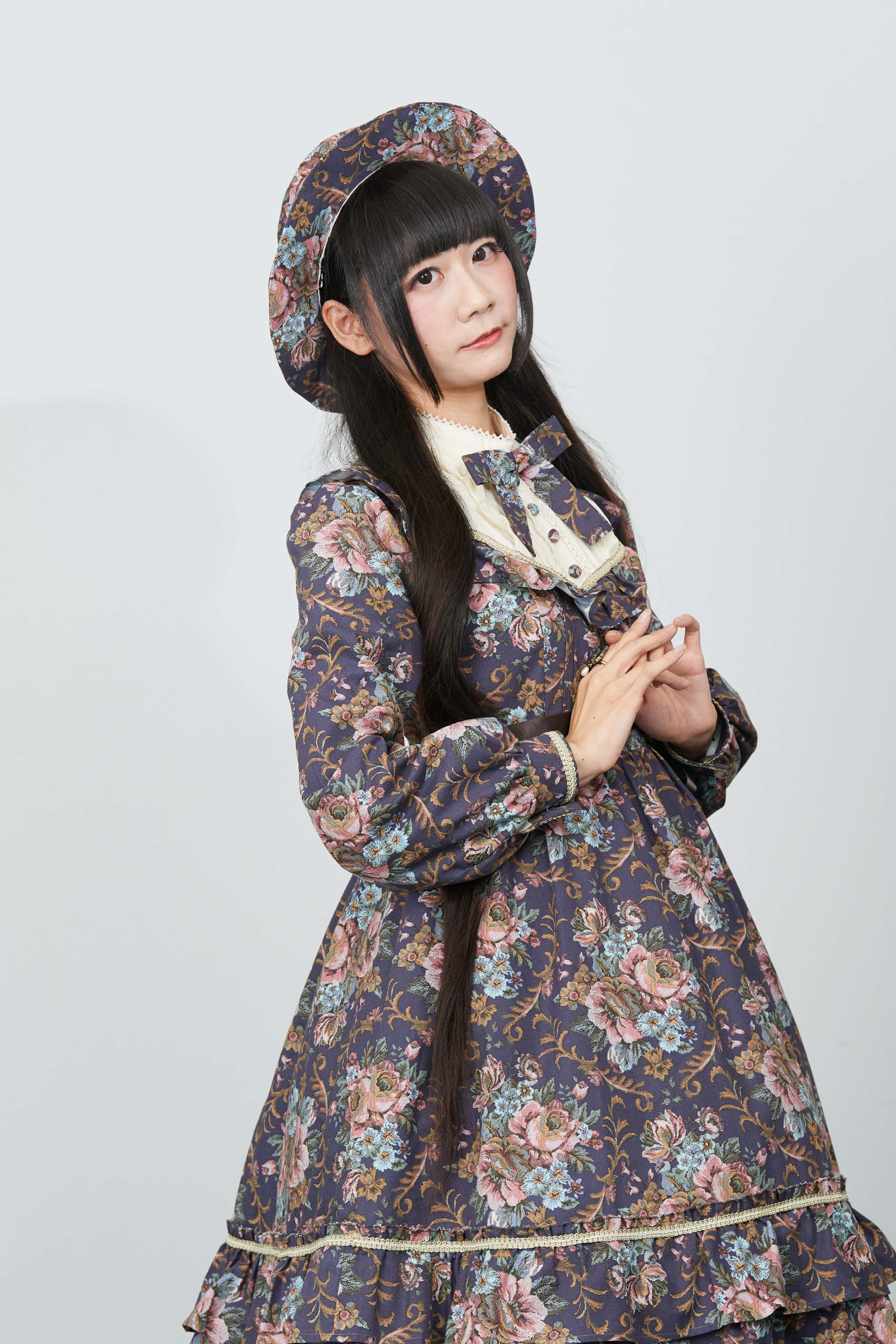 Lolita Fashion 桌布 壁紙 — 一位年輕女性身穿花卉圖案的洛麗塔連衣裙和相配的帽子，在純白背景前優雅地擺姿勢。