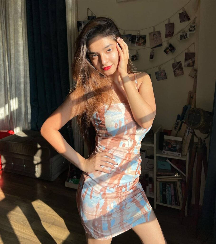 Indian 桌布 壁紙 — 一位年輕女性身穿藍色和蜜桃色紮染連衣裙，在陽光充足的房間裡自信地擺姿勢，身後牆上掛著照片。