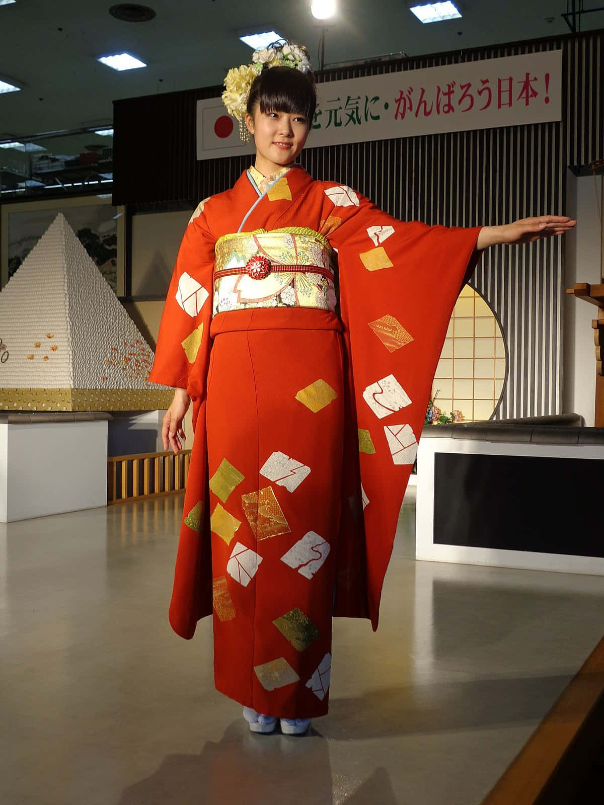 Kimono 桌布 壁紙 — 一位年輕女性身穿鮮紅色和服，帶有金色和白色的信封圖案，在明亮的燈光下優雅地在室內擺姿勢。