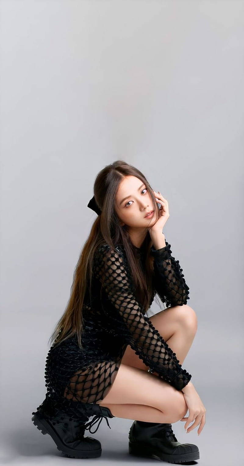 jisoo 可愛 桌布 壁紙 — 一位年輕女性身穿黑色魚網裙和戰鬥靴，蹲在純灰色攝影棚背景前，若有所思地凝視鏡頭。