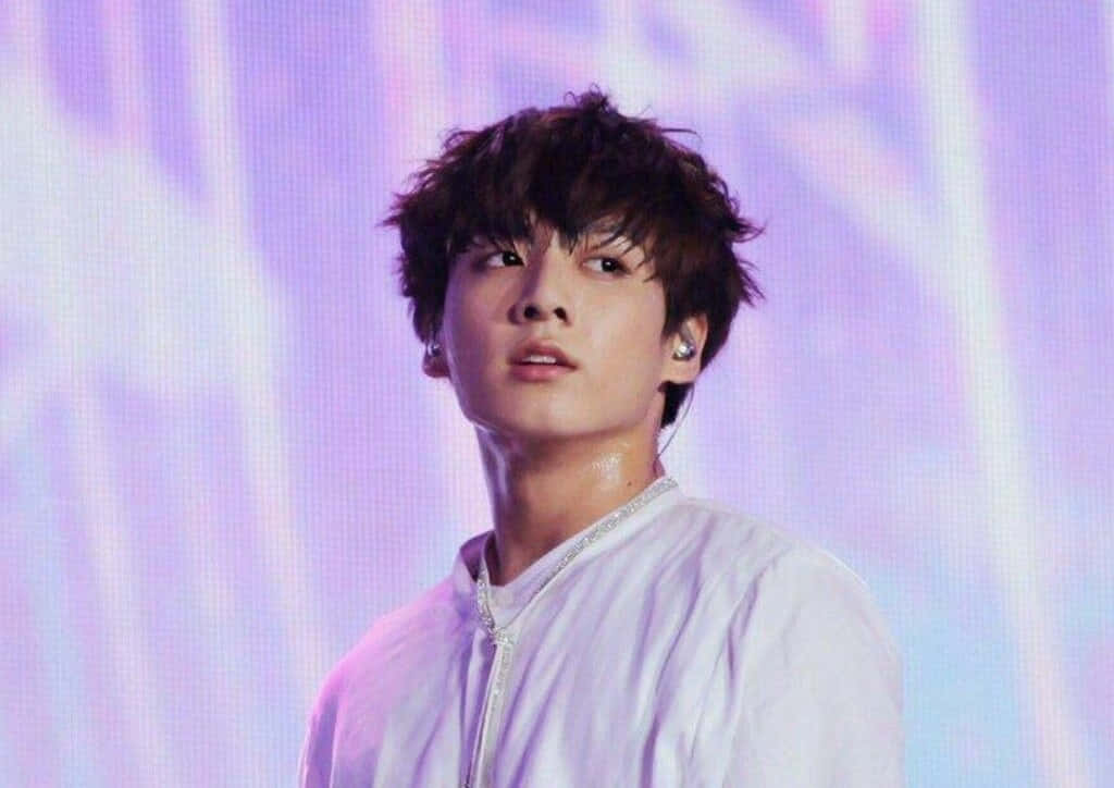 Jungkook 桌布 壁紙 — 一位年輕男子，一頭凌亂的黑髮，在充滿活力的紫色和藍色舞台燈光下表演。
