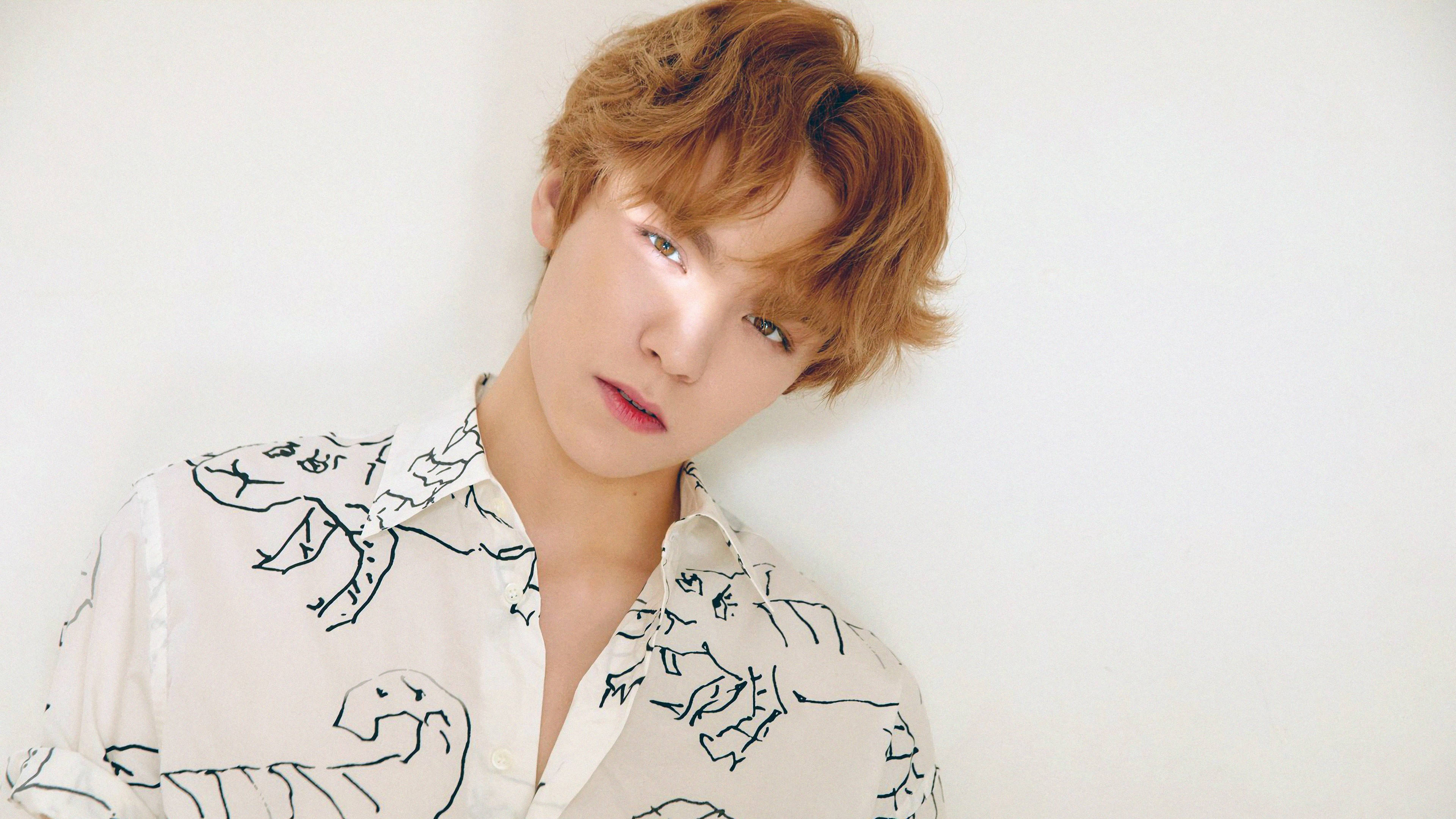 Vernon 桌布 壁紙 — 一位年輕男子，一頭蓬鬆的紅髮，靠在一面純白牆上，身穿帶有黑色恐龍圖案的米色襯衫。