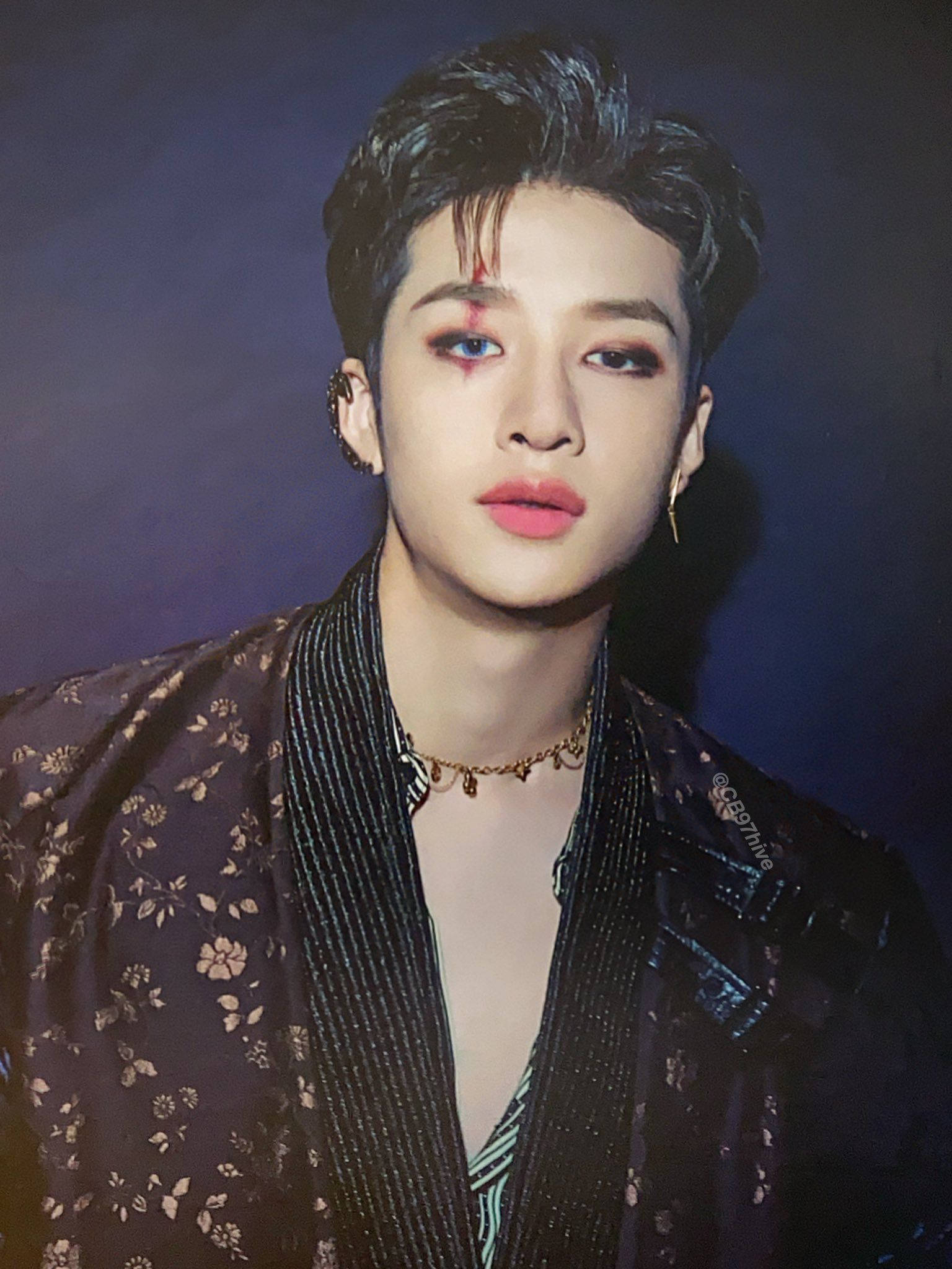 Stray Kids 桌布 壁紙 — 一位年輕男子，帶有戲劇性的眼妝和花卉圖案外套，在深藍色背景前擺姿勢。
