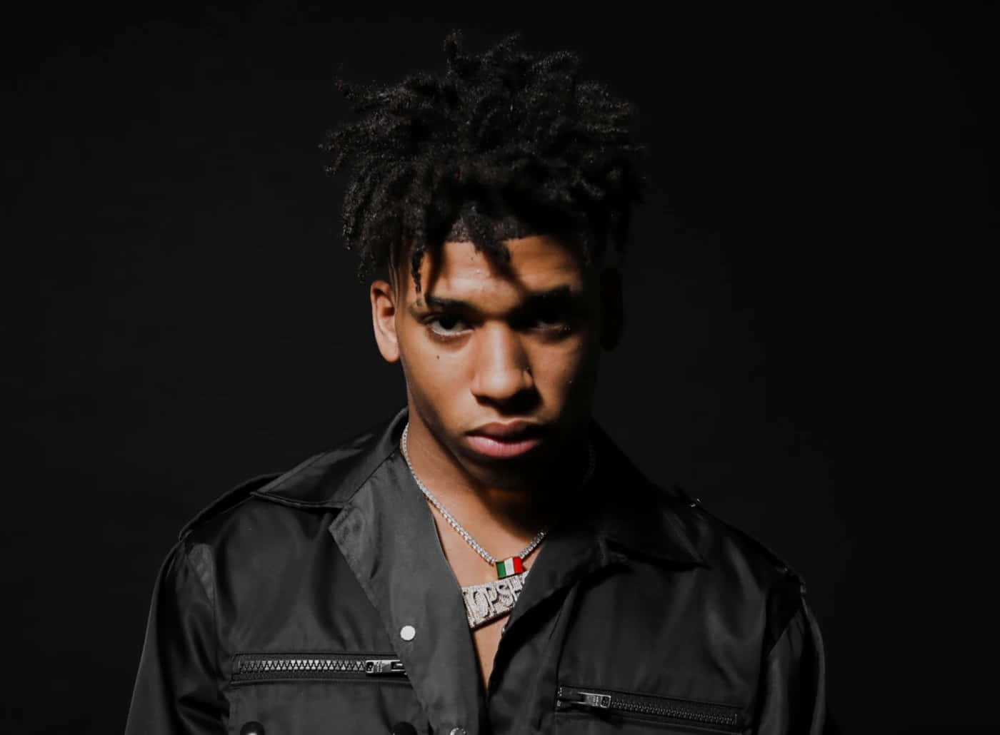 年輕男子身穿黑色外套和銀色鏈條，在攝影棚中目光銳利 — NLE Choppa GIF 壁紙