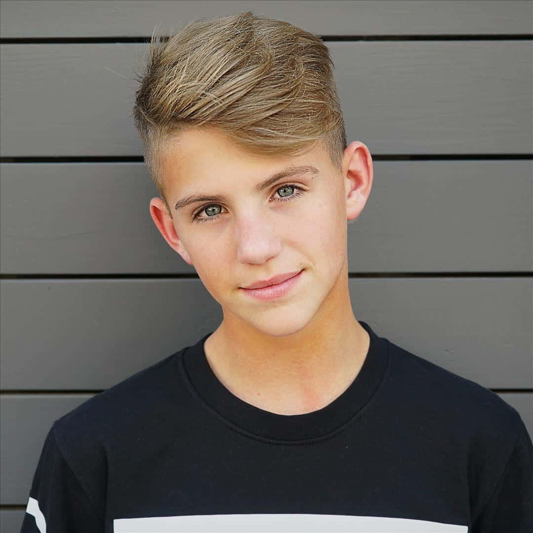 Matty B 桌布 壁紙 — 一位年輕男子，擁有造型金髮和綠色眼睛，對著灰色木板牆溫柔微笑。