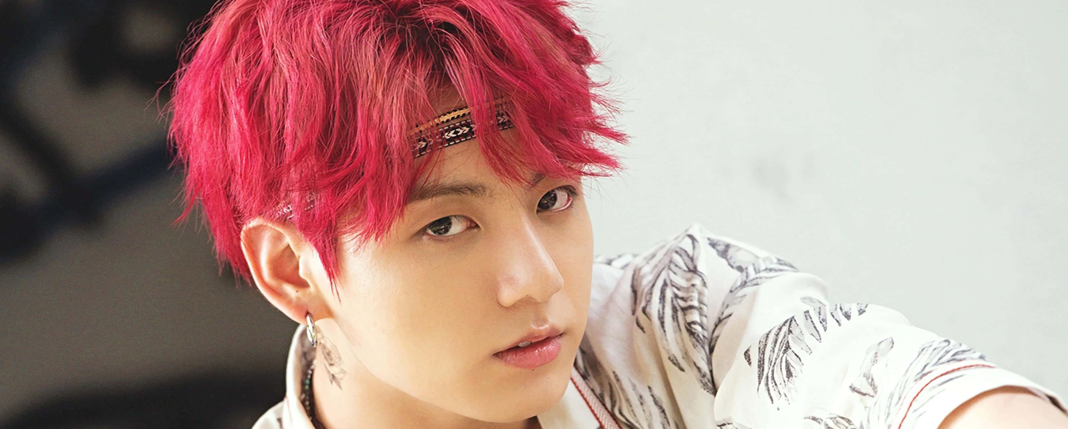 Jungkook 桌布 壁紙 — 一位年輕男子，擁有鮮豔的粉紅色頭髮和圖案襯衫，在柔和模糊的背景前凝視著相機。