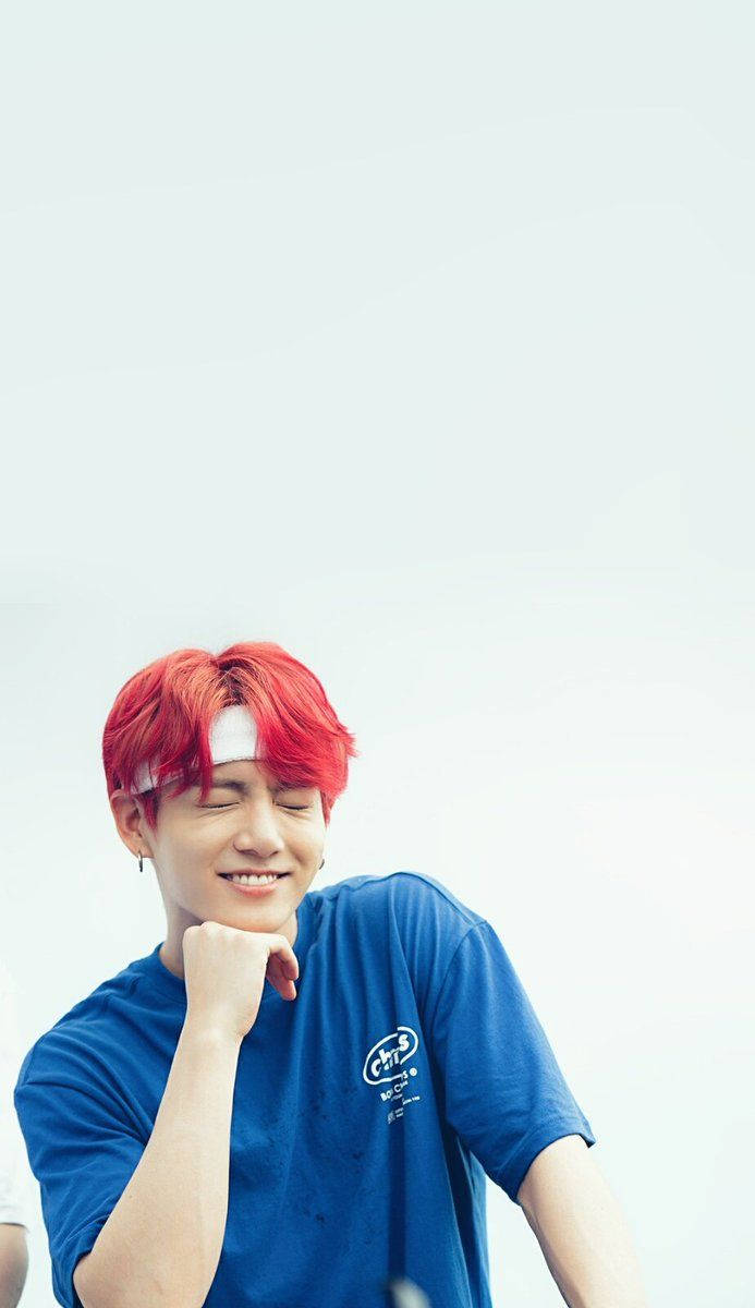 BTS 桌布 壁紙 — 一位年輕男子，擁有鮮豔的紅髮和白色頭帶，在純色淺色背景前，托腮微笑，表情俏皮。