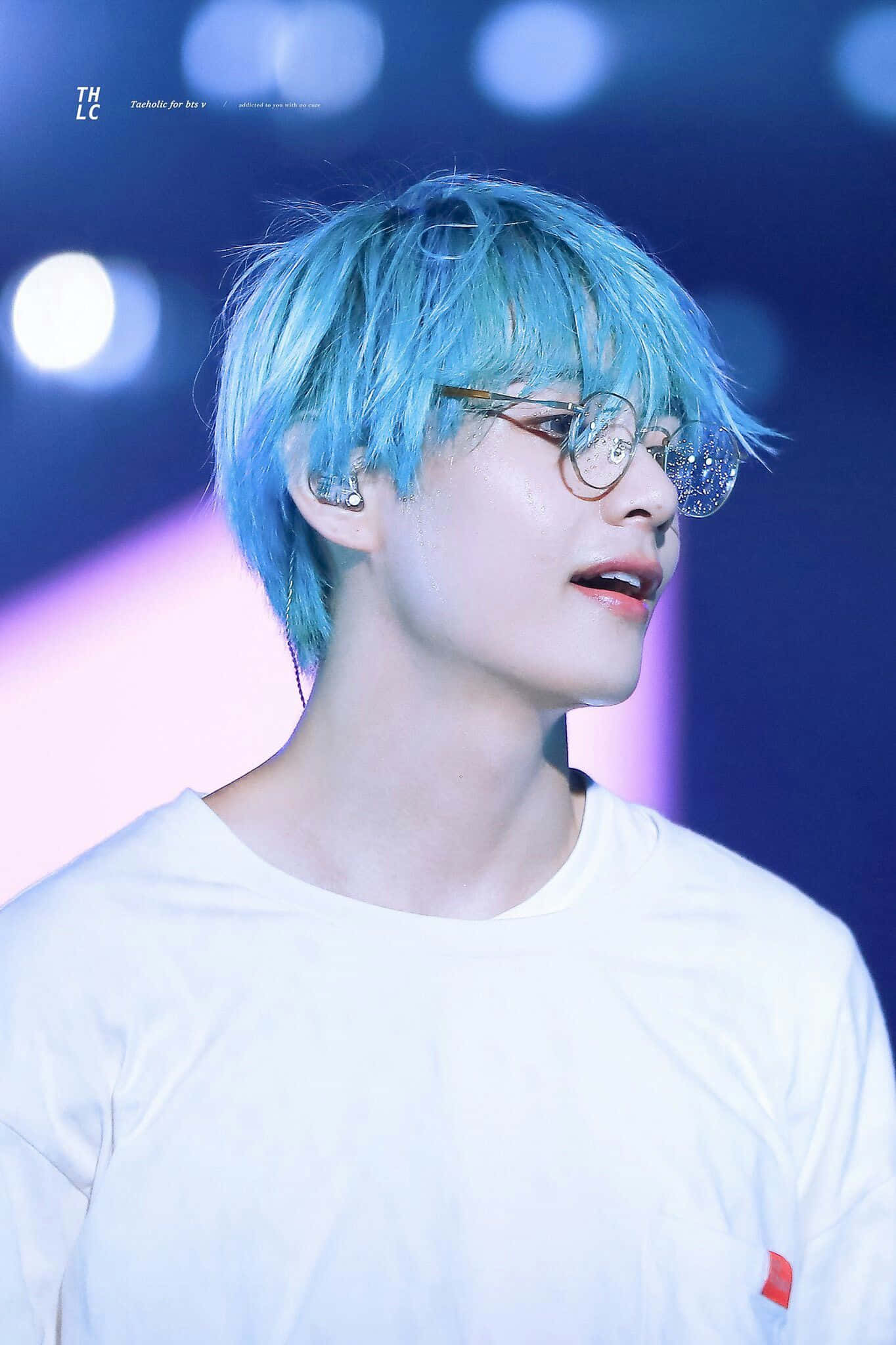 Taehyung Cute 桌布 壁紙 — 一位年輕男子，擁有鮮豔的藍色頭髮和圓框眼鏡，在舞台燈光下穿著白色T恤向上看。