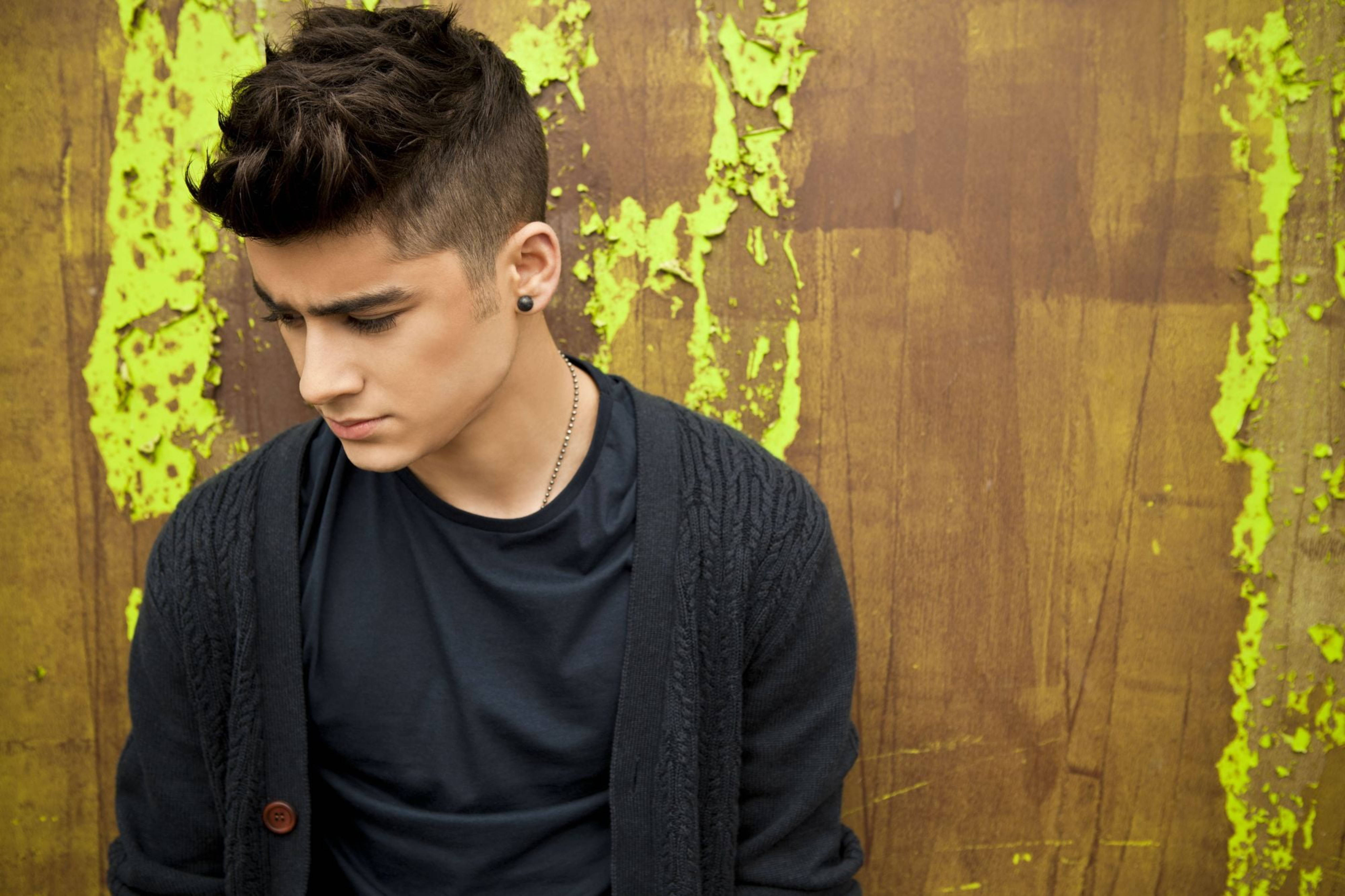 zayn 桌布 壁紙 — 一位年輕男子，梳著深色造型頭髮，戴著耳環，低頭看著一面破舊的木牆，牆上剝落的霓虹綠色油漆。
